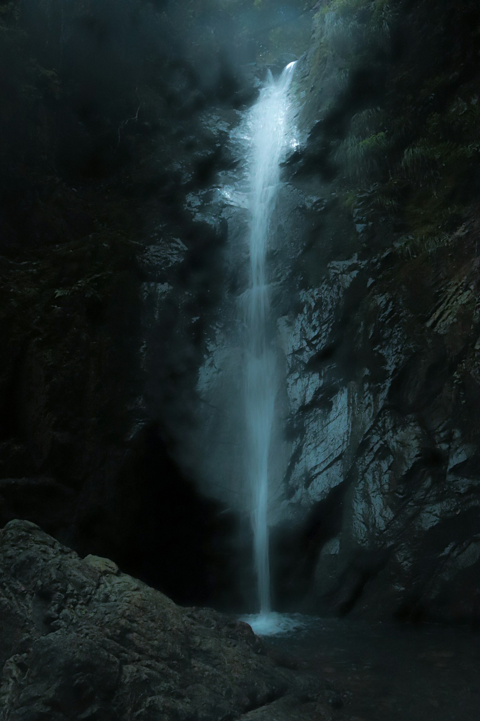 A tranquil waterfall cascading down a rocky cliff in a dark forest