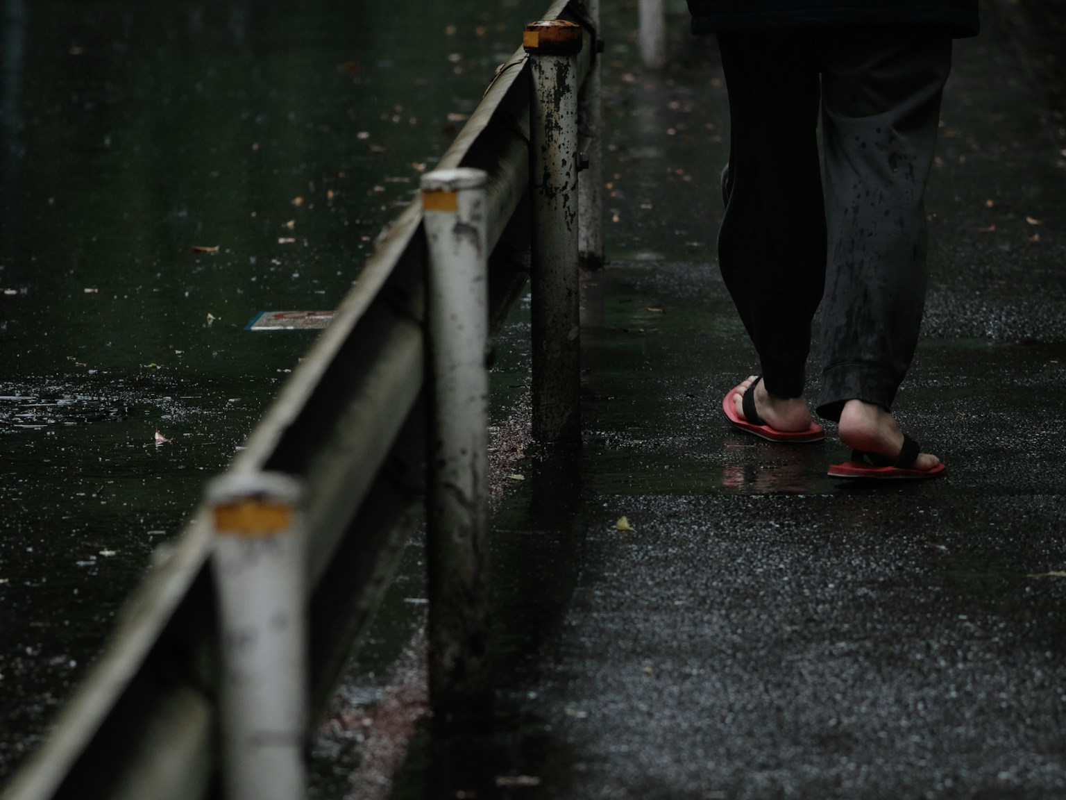 Person walking on a wet sidewalk with flip-flops in the rain