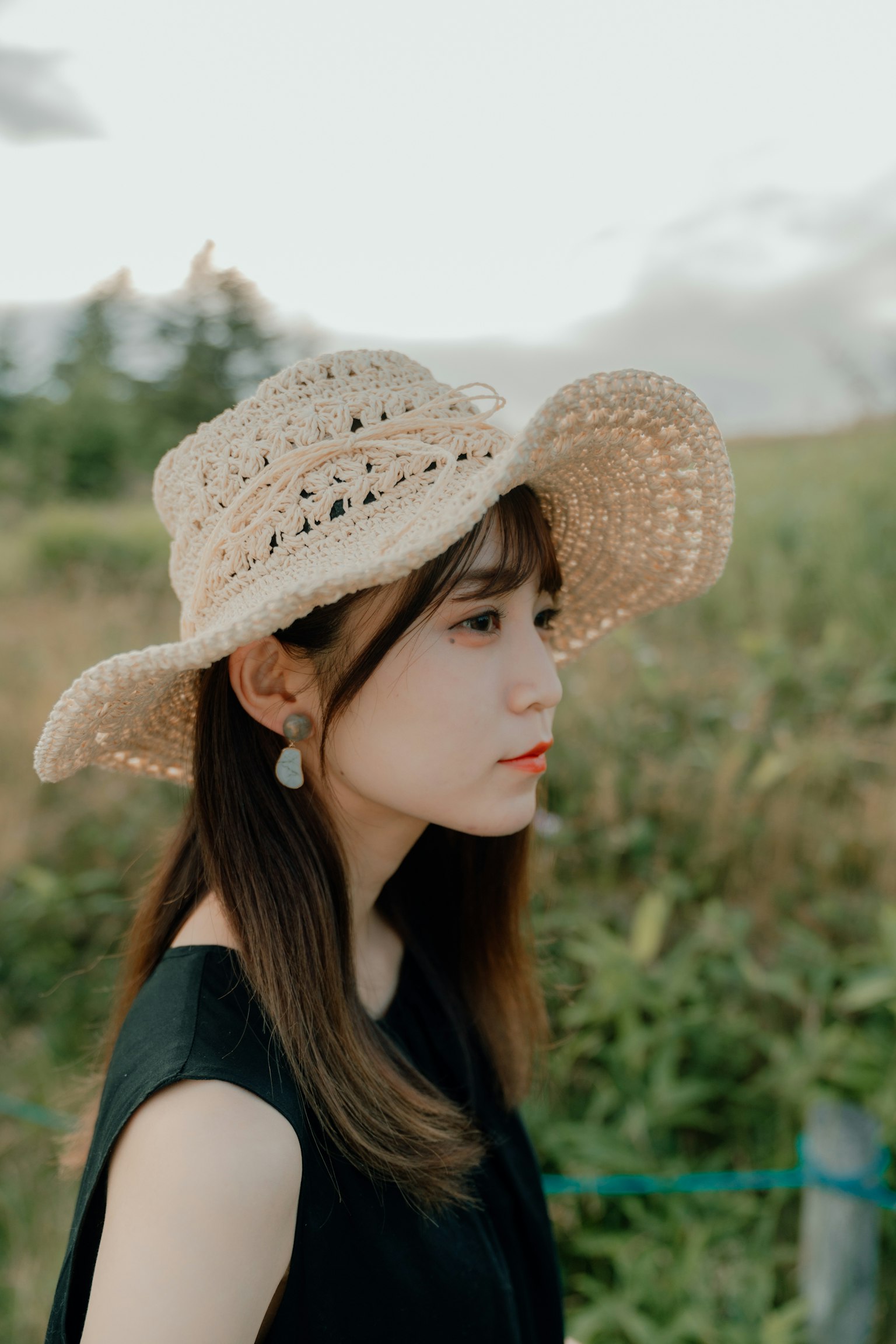 A woman wearing a straw hat standing sideways with green grass and sky in the background