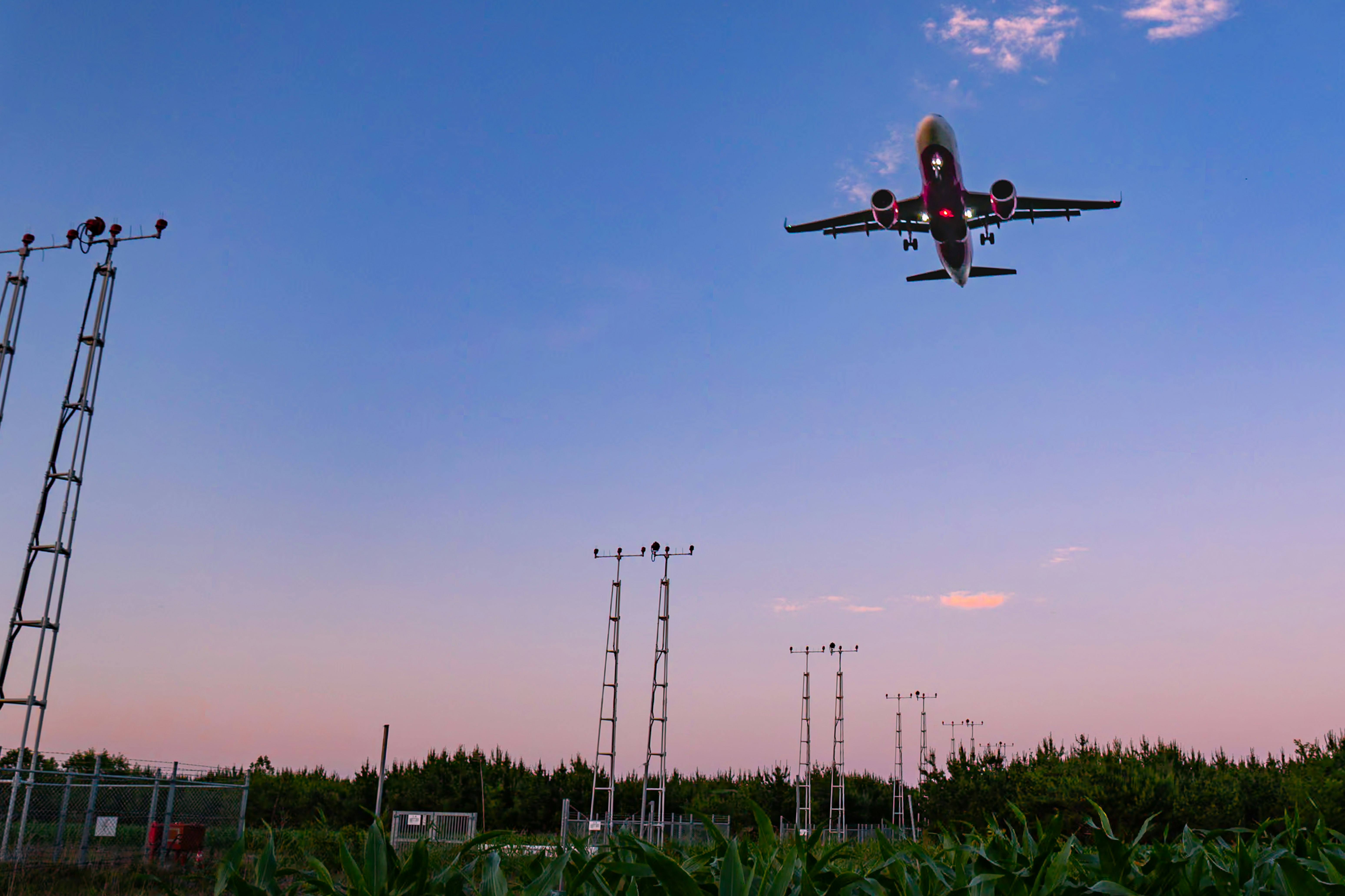 夕暮れの空に飛ぶ旅客機と通信アンテナ