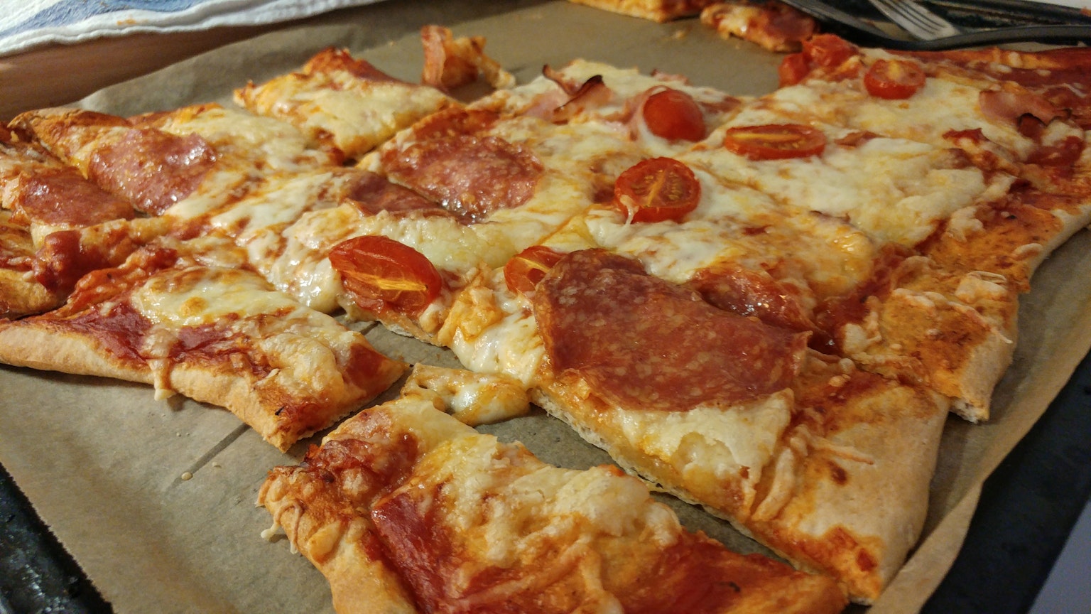 Pizza appena sfornata su un vassoio con pomodori e formaggio