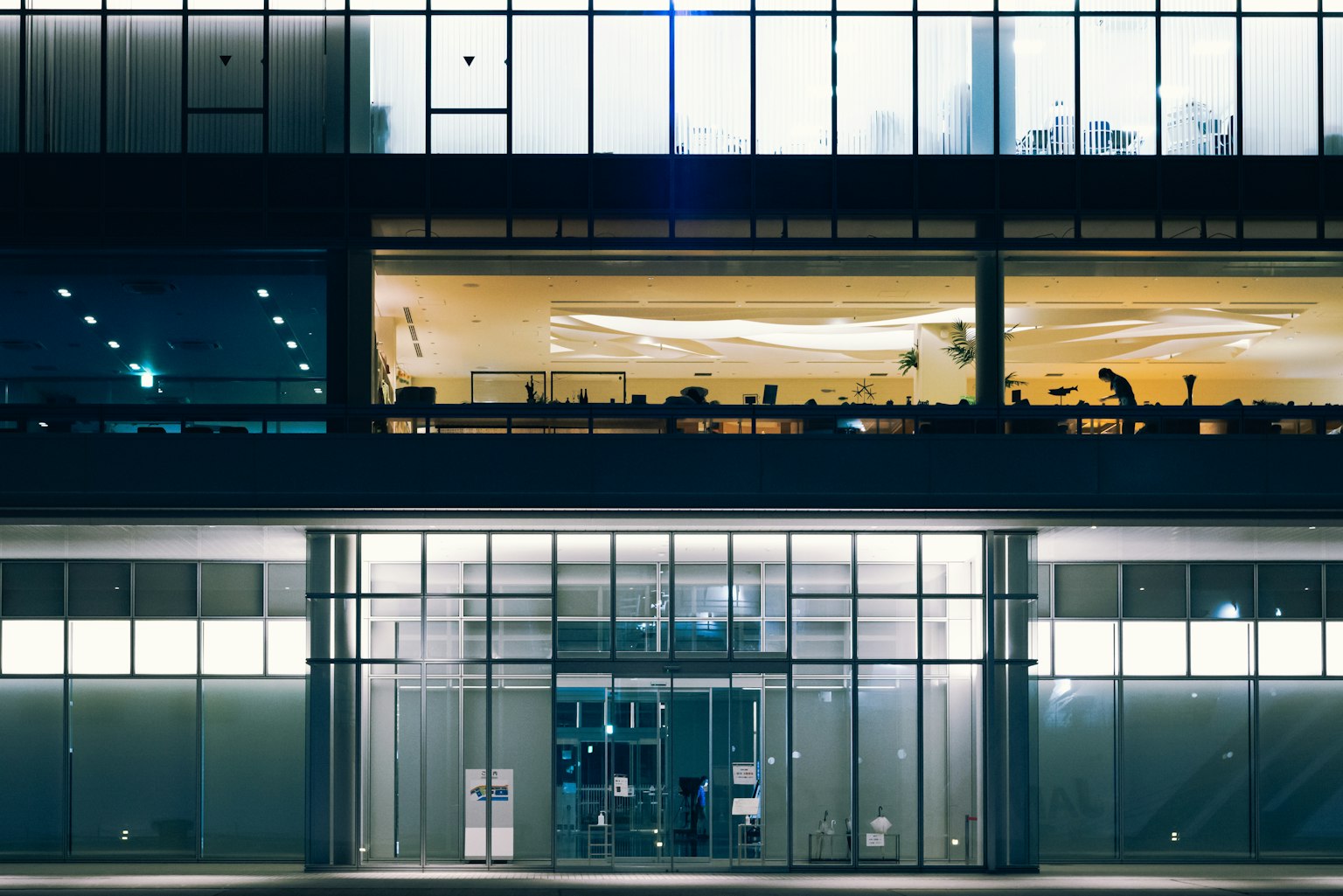 Facciata moderna di un edificio di notte con grandi finestre di vetro che mostrano un interno illuminato