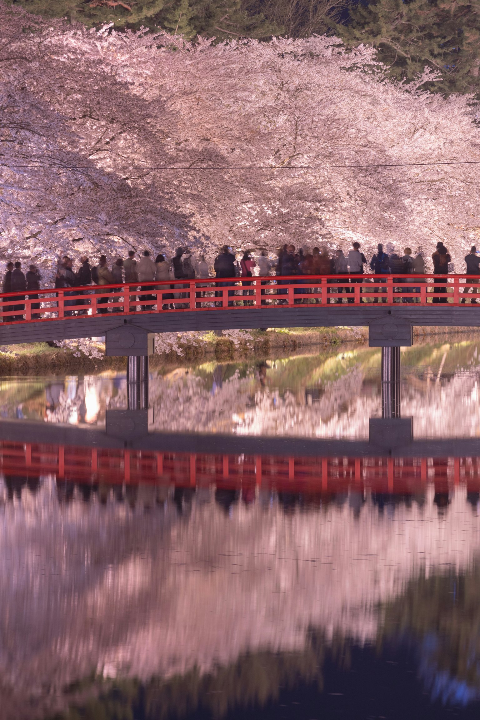 Vue pittoresque d'un pont rouge avec des touristes réfléchis dans l'eau