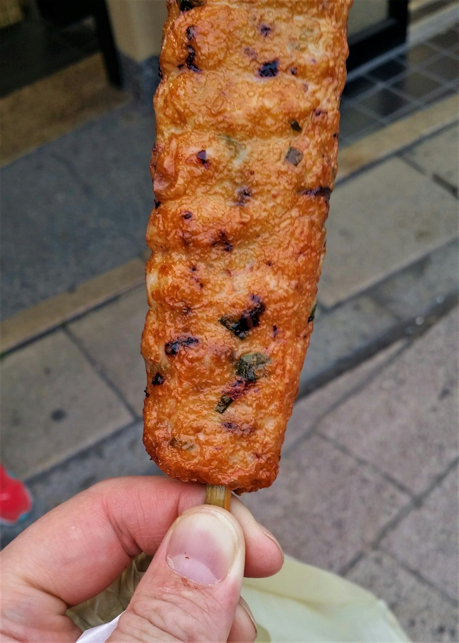 Una mano che tiene uno snack grigliato su uno spiedino con superficie dorata