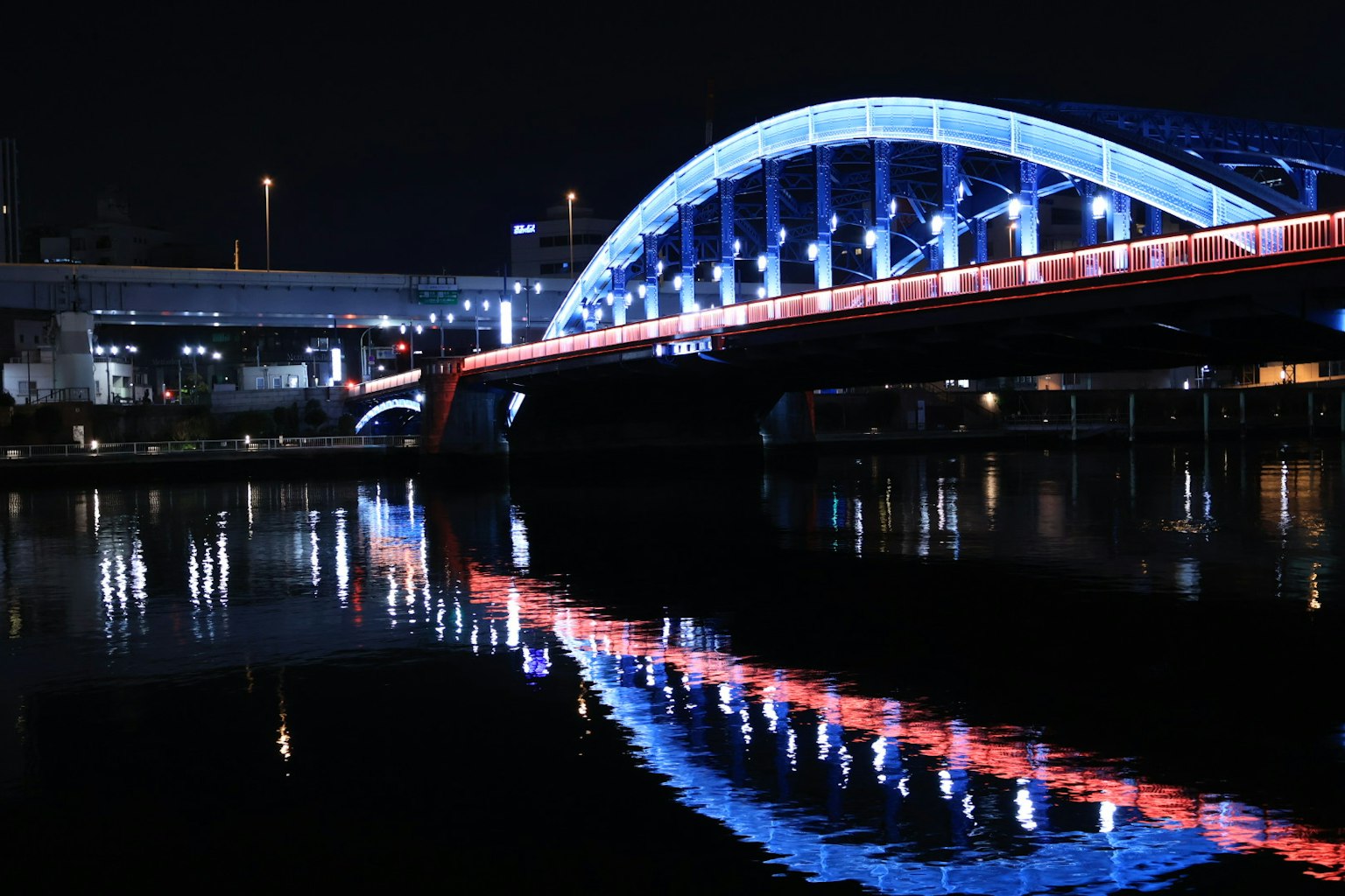 A beautiful arch bridge illuminated in blue and red lights over a river at night