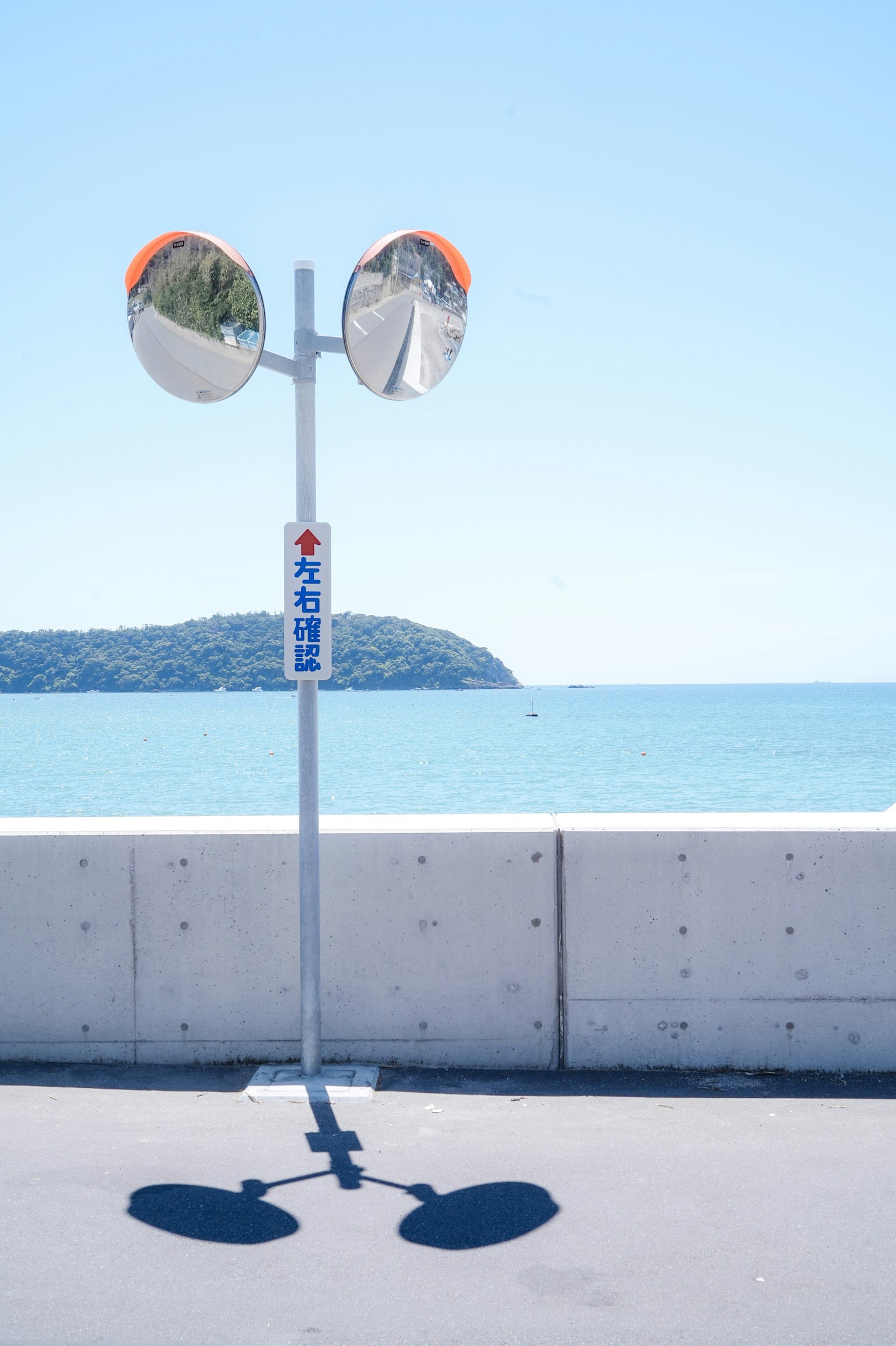 Segnale stradale con due specchi sullo sfondo di un mare blu e un'isola