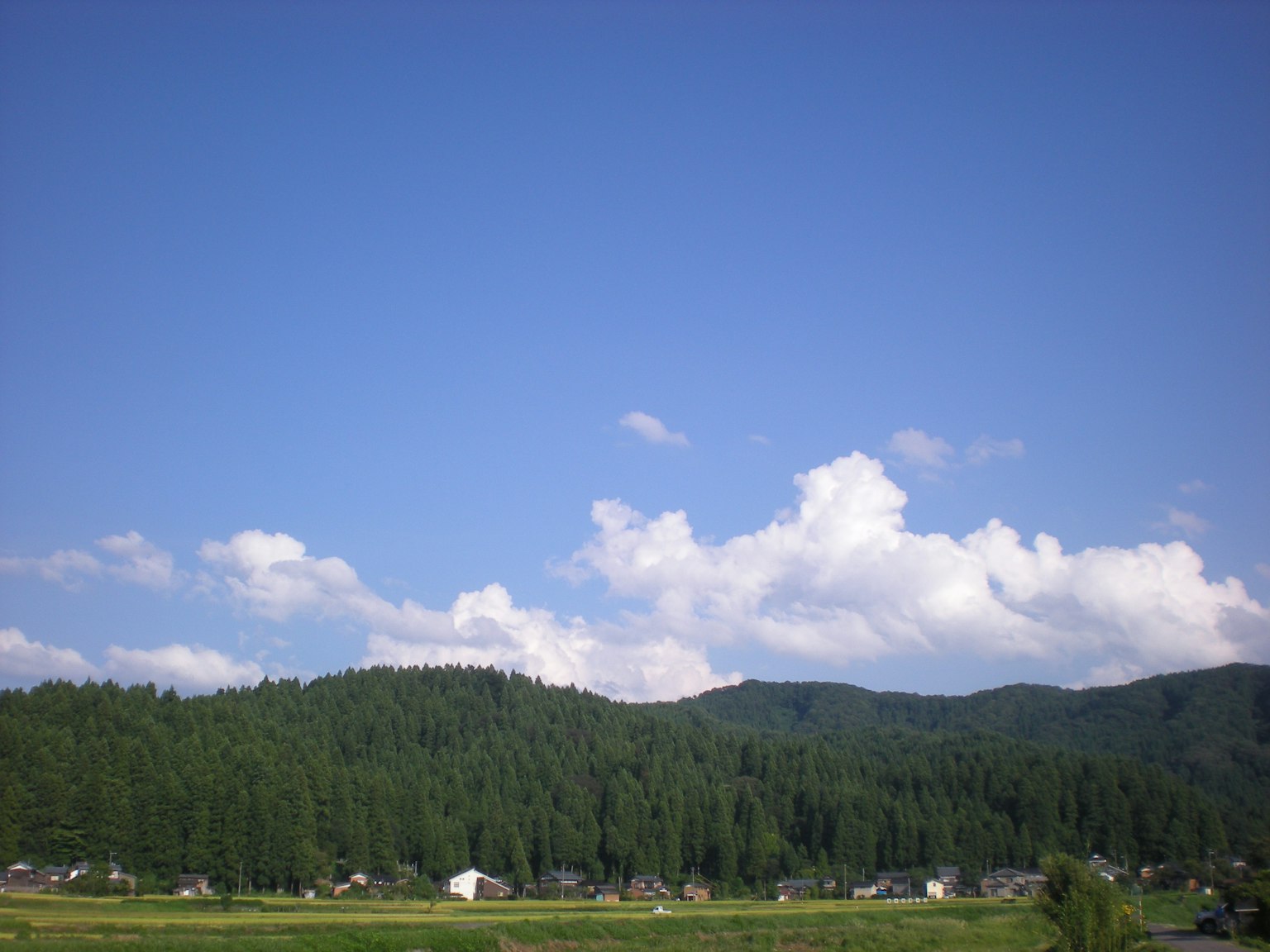 Rural landscape featuring blue sky and white clouds green mountains and scattered houses