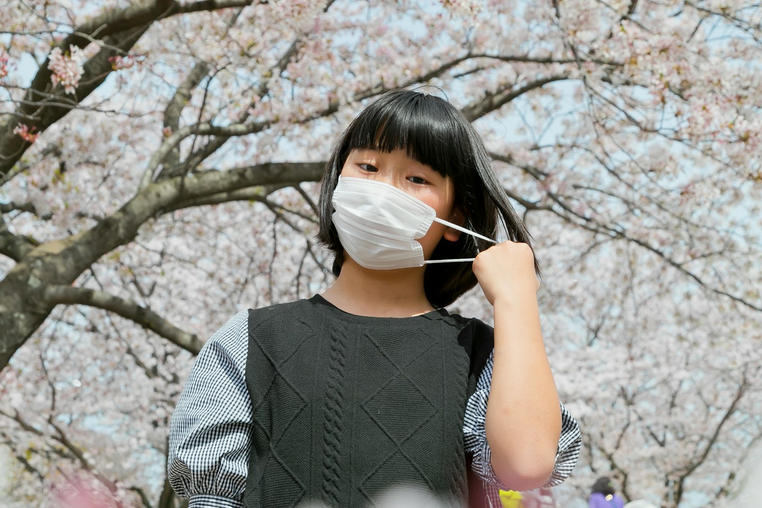 A girl wearing a mask posing under a cherry blossom tree