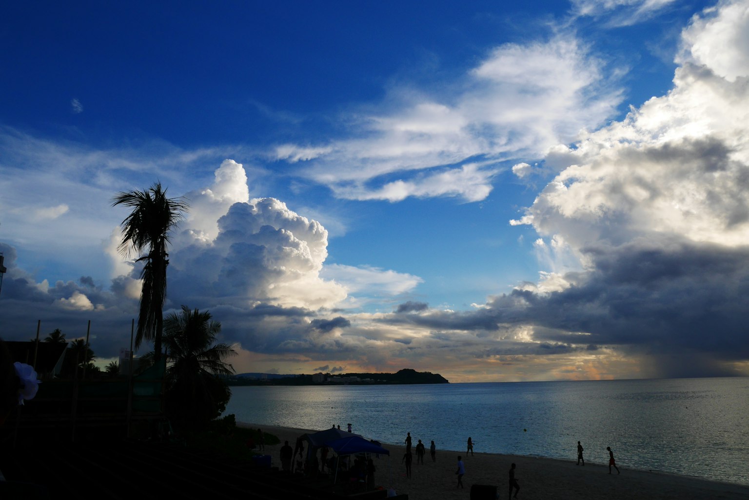Scenic beach view with blue sky and white clouds at sunset featuring silhouettes of people