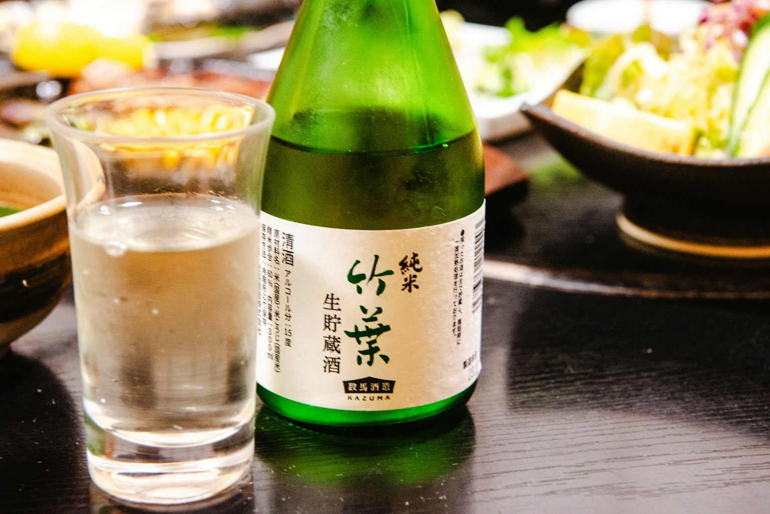 Chai rượu sake Nhật Bản màu xanh và cốc trong suốt trên bàn có các món ăn xung quanh