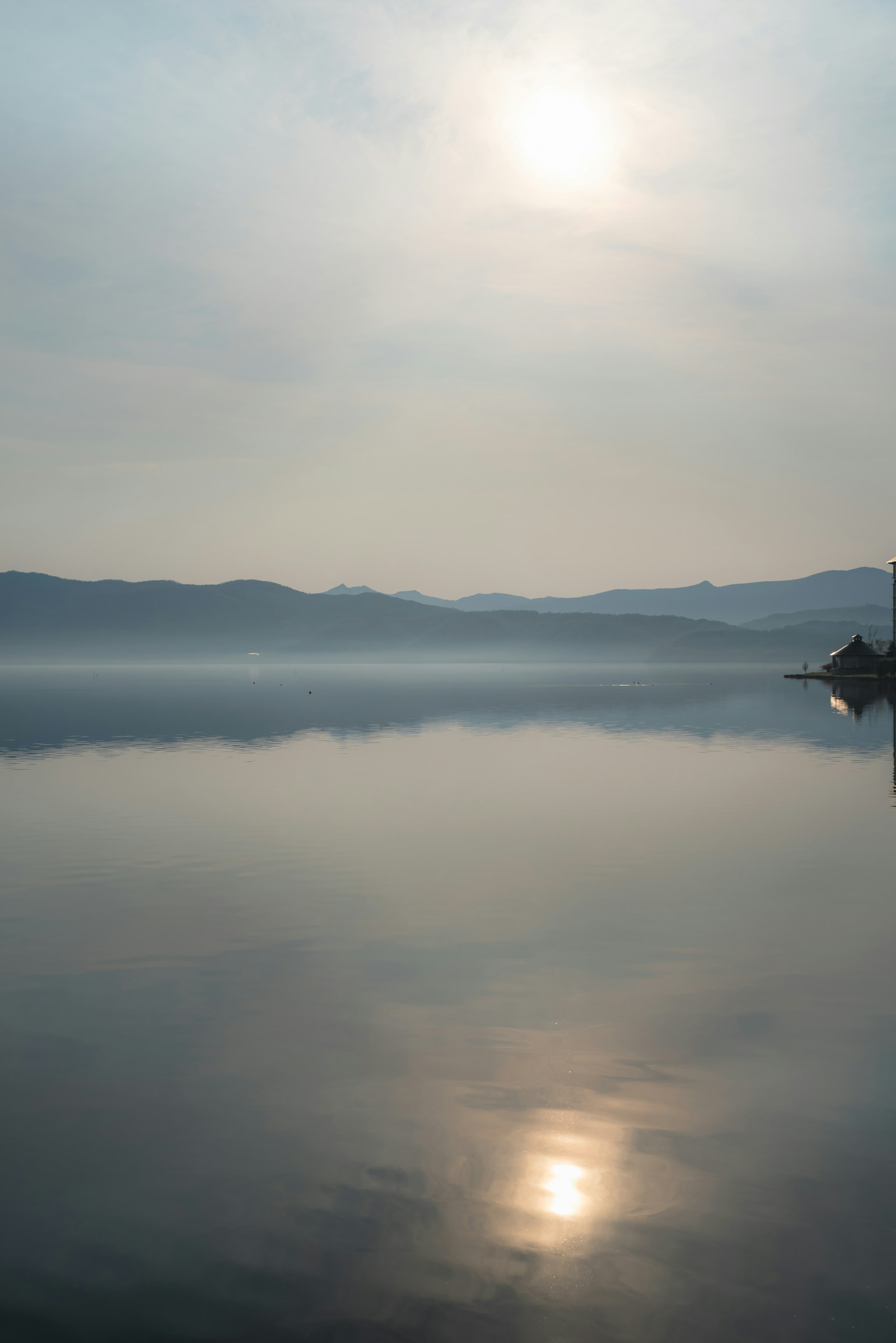 Lago calmo che riflette la luce del sole e un paesaggio nebbioso
