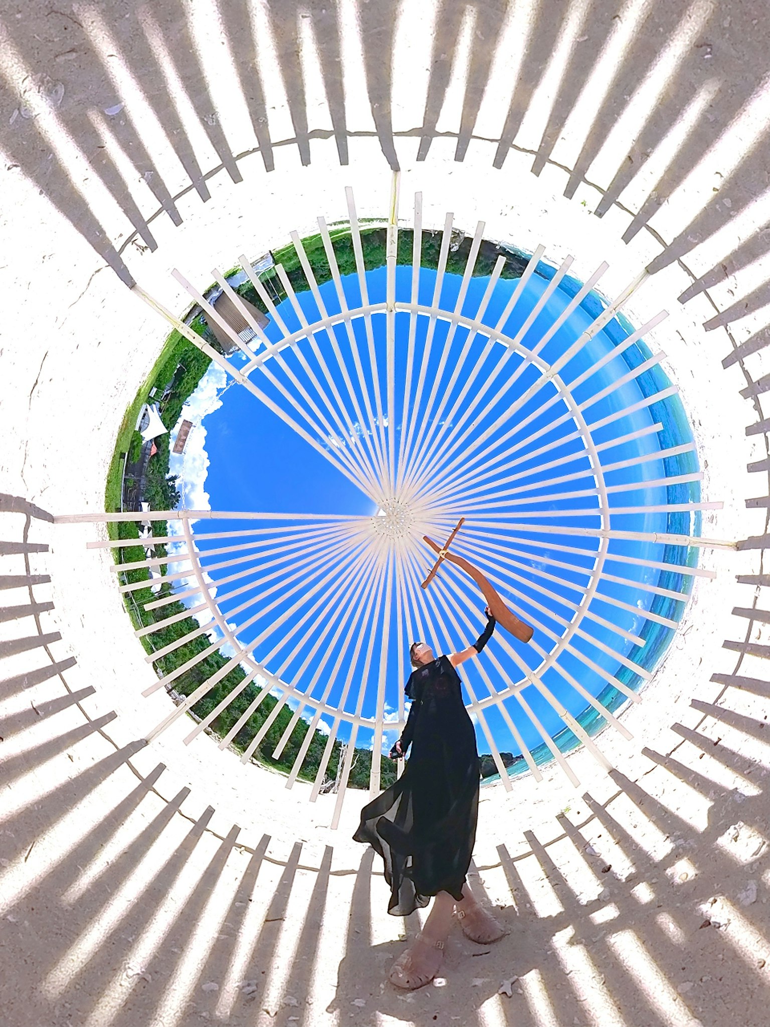 Immagine di una persona che si trova sotto una struttura circolare con cielo blu e paesaggio verde sullo sfondo