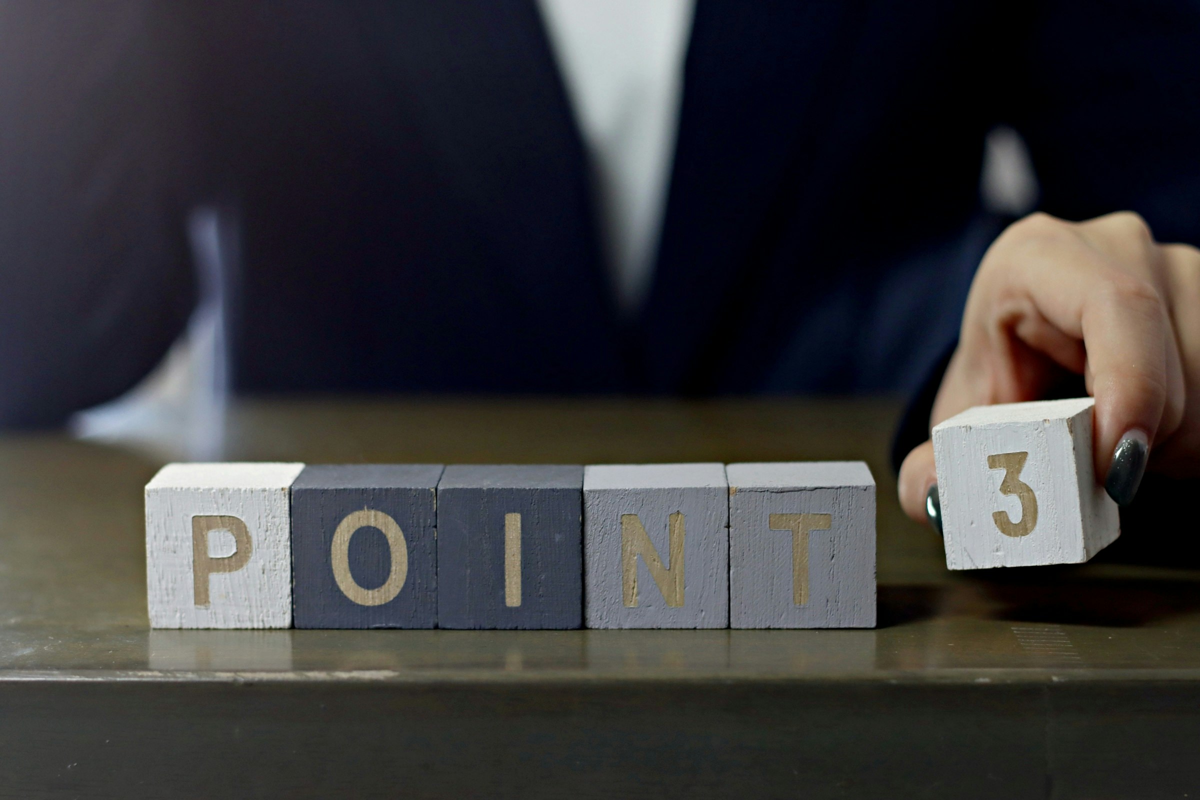Buchstabenblöcke auf einem Schreibtisch mit „POINT“ und Hand mit Würfel „3“