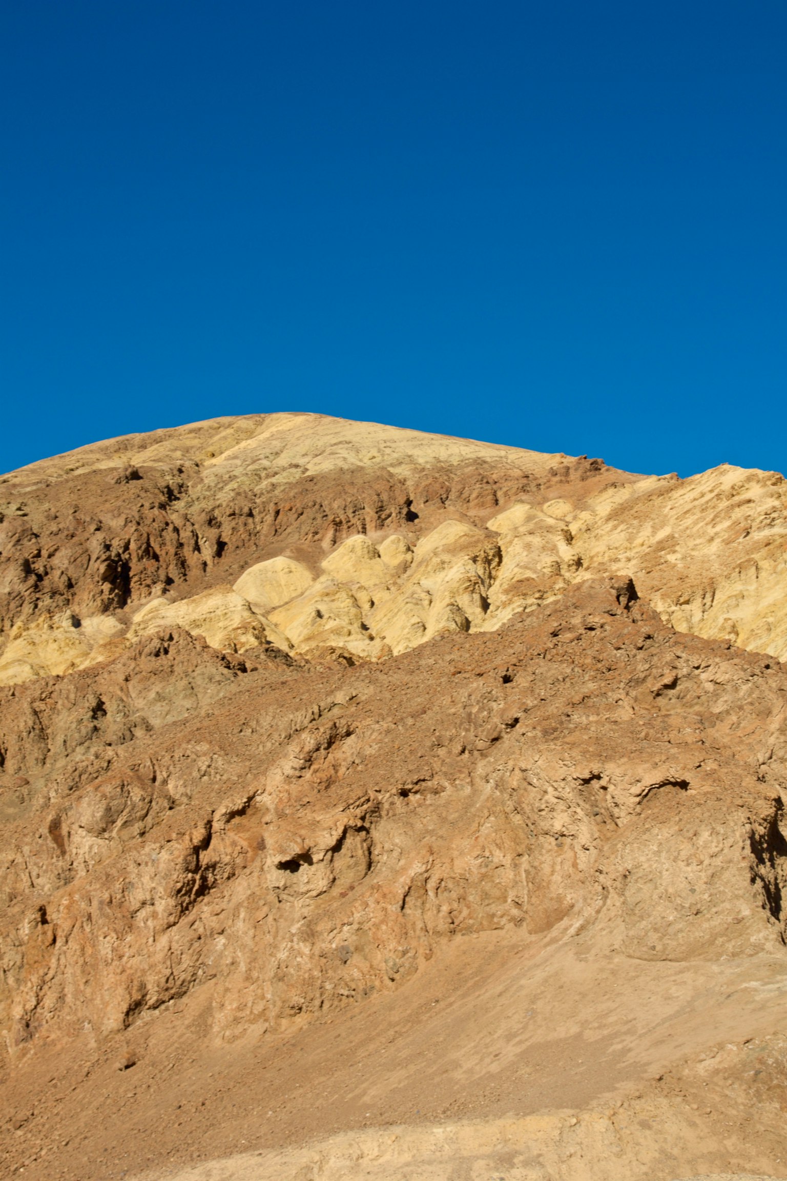 Montaña con formaciones rocosas marrones y amarillas bajo un cielo azul