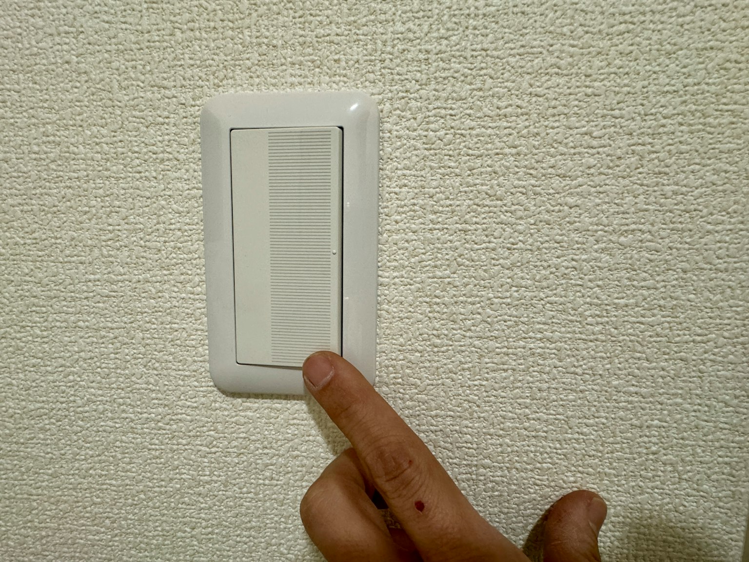 一个手指按在纹理墙上的白色开关上
