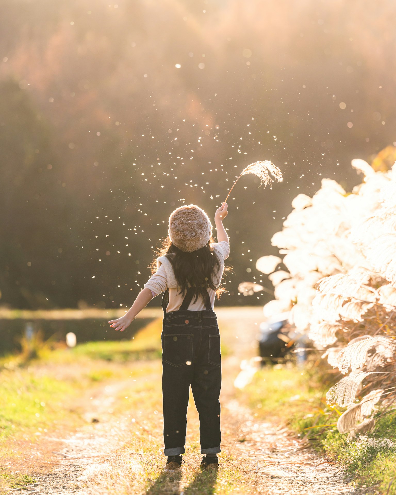 Child joyfully splashing water on a sunlit path surrounded by greenery