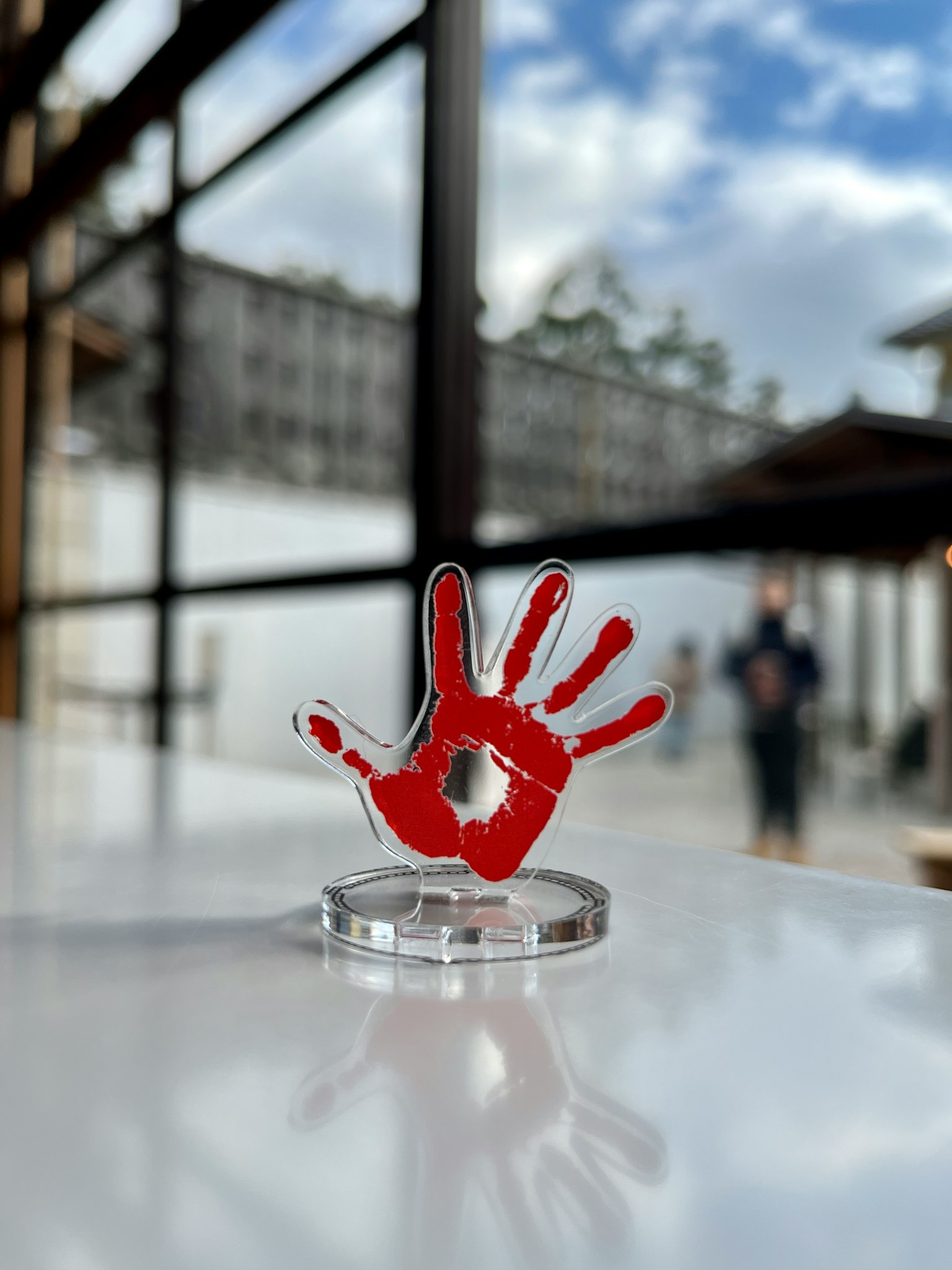 Una escultura de huella roja sobre una base transparente colocada en una mesa con un cielo nublado de fondo