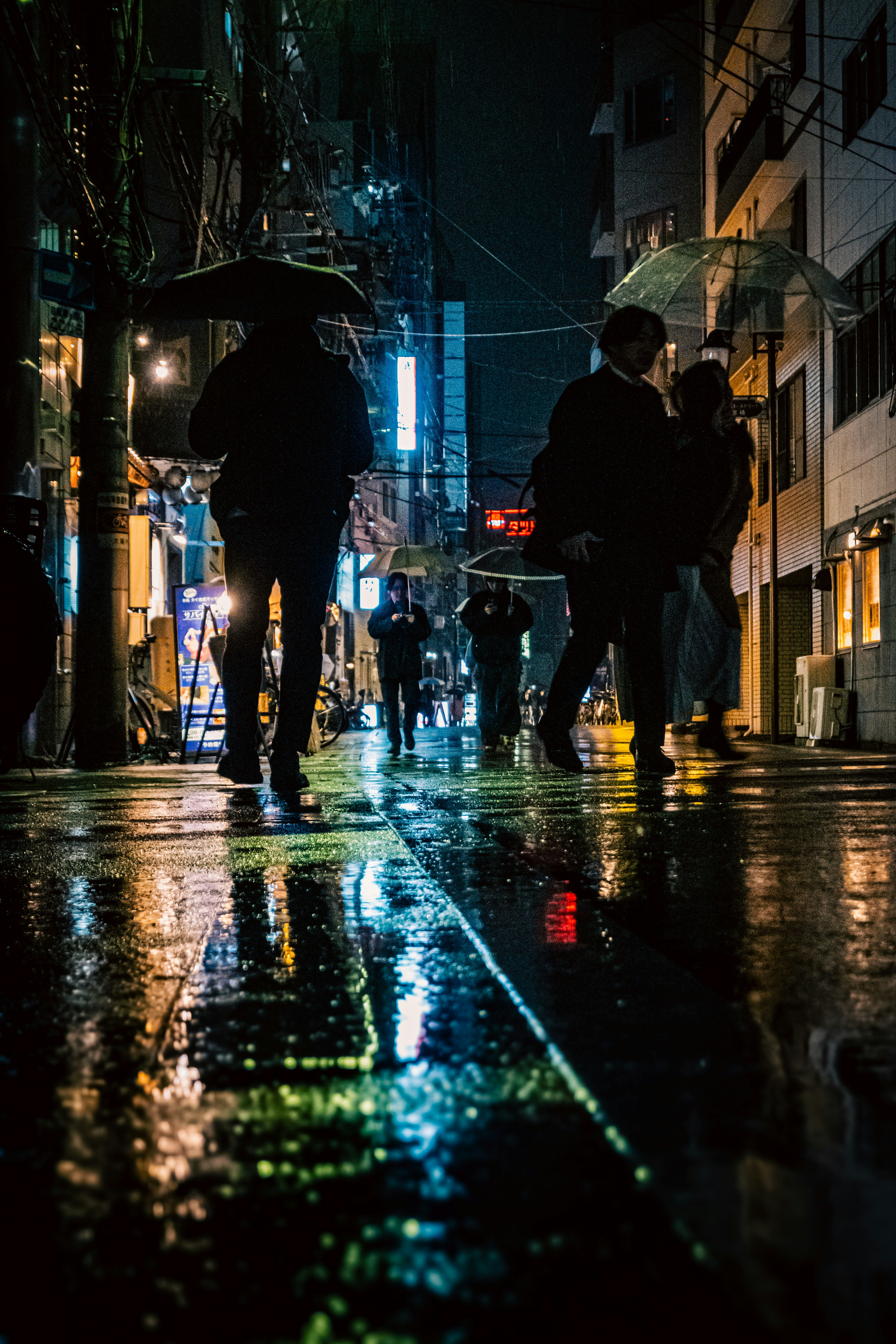 雨の路地で傘をさす人々の夜景