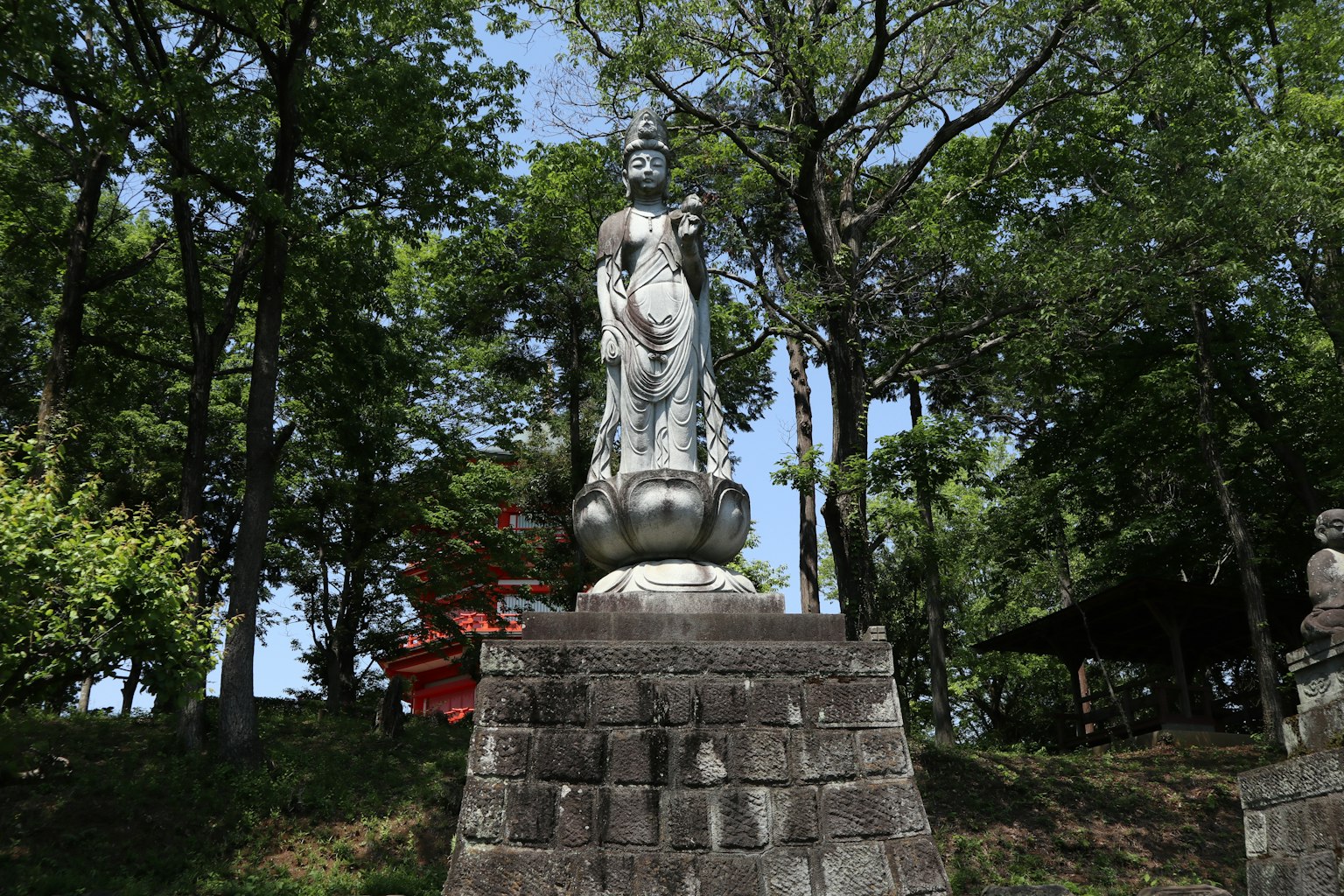 Statue de Kannon se tenant parmi des arbres verdoyants