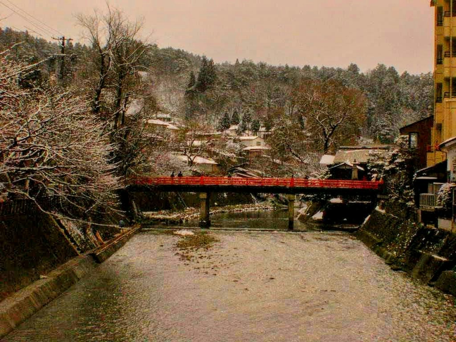 Fiume coperto di neve con un ponte rosso e case circostanti