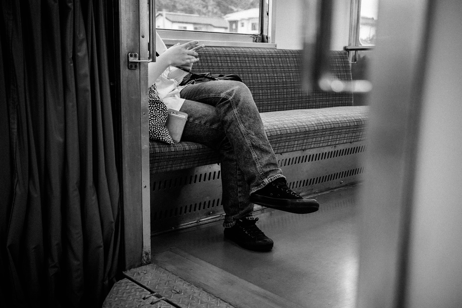 Une personne assise dans un train avec les jambes et les mains visibles en noir et blanc