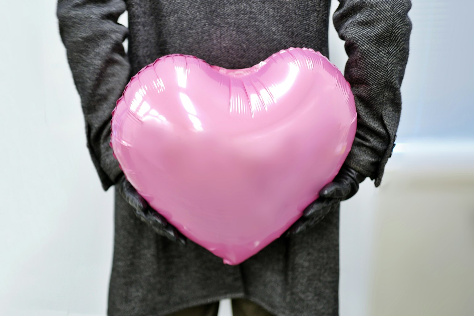 Eine Person hält einen pinkfarbenen herzförmigen Ballon hinter ihrem Rücken