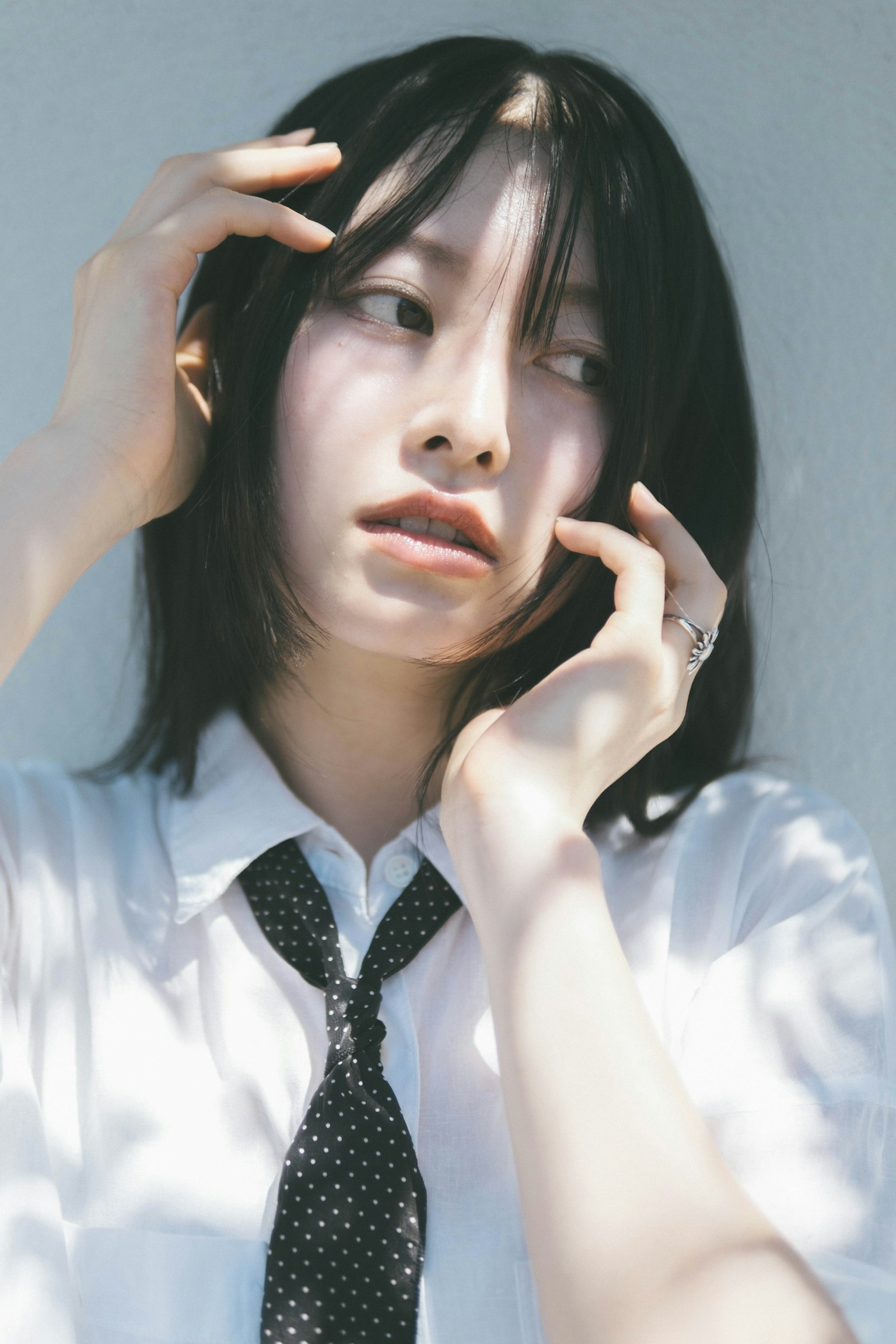 一位黑髮女性穿著白襯衫和黑領帶，思考時觸摸著自己的頭髮