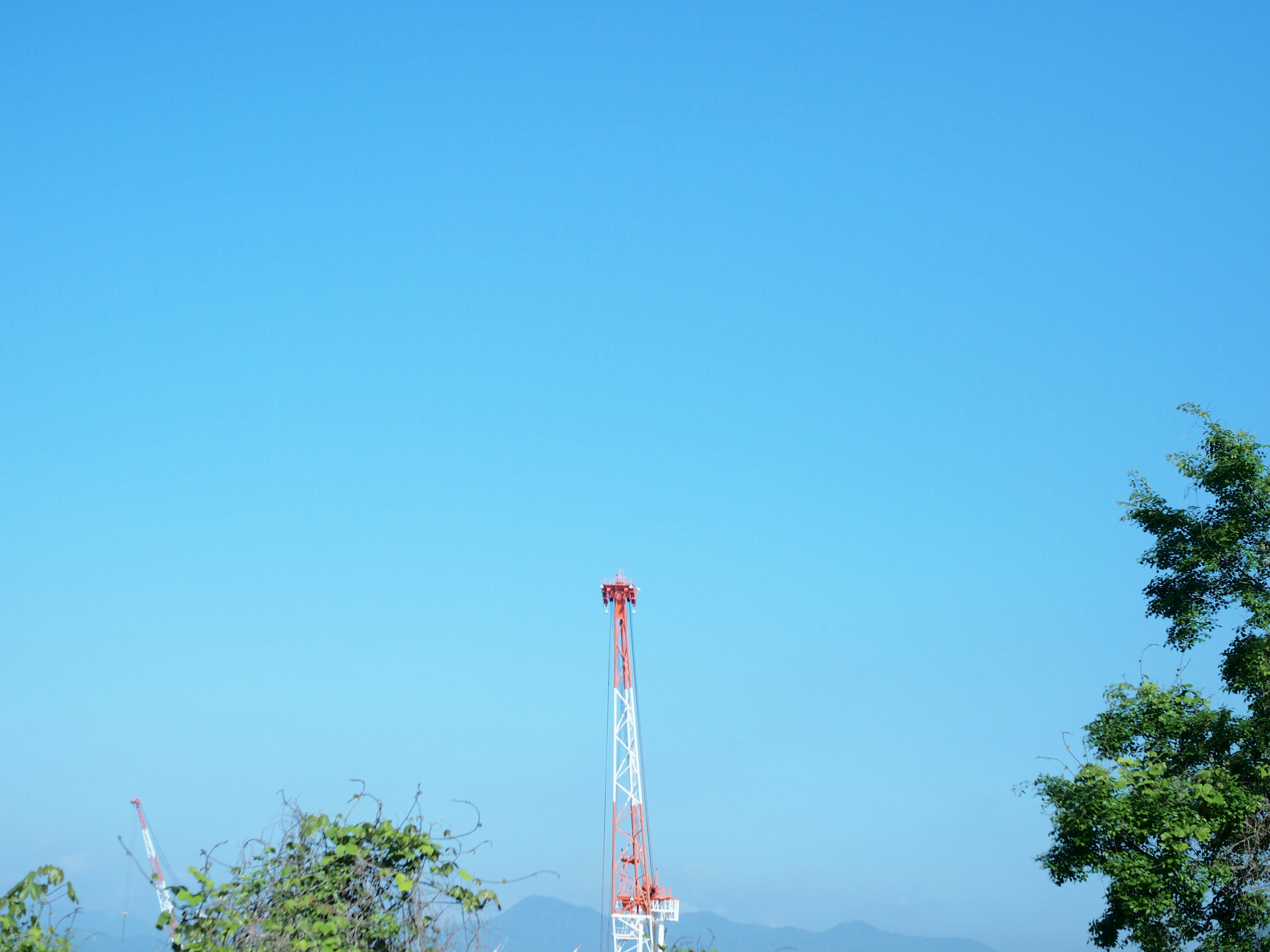 Torre de comunicación roja y blanca contra un cielo azul con montañas