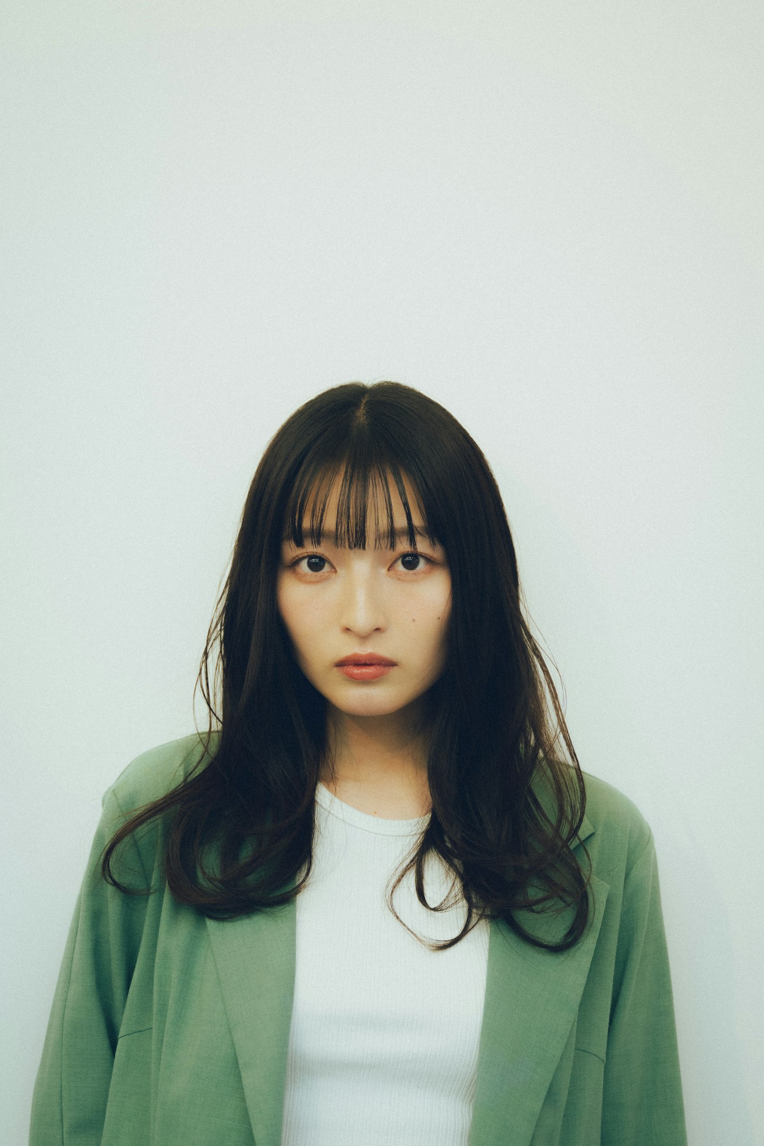 흰색 배경 앞에 서 있는 녹색 재킷을 입은 여성의 초상화
