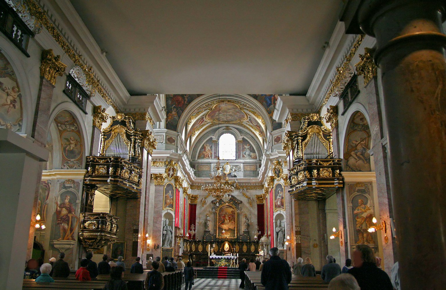 Intérieur d'une belle église baroque avec un plafond grand et des colonnes décoratives avec un autel et des personnes visibles