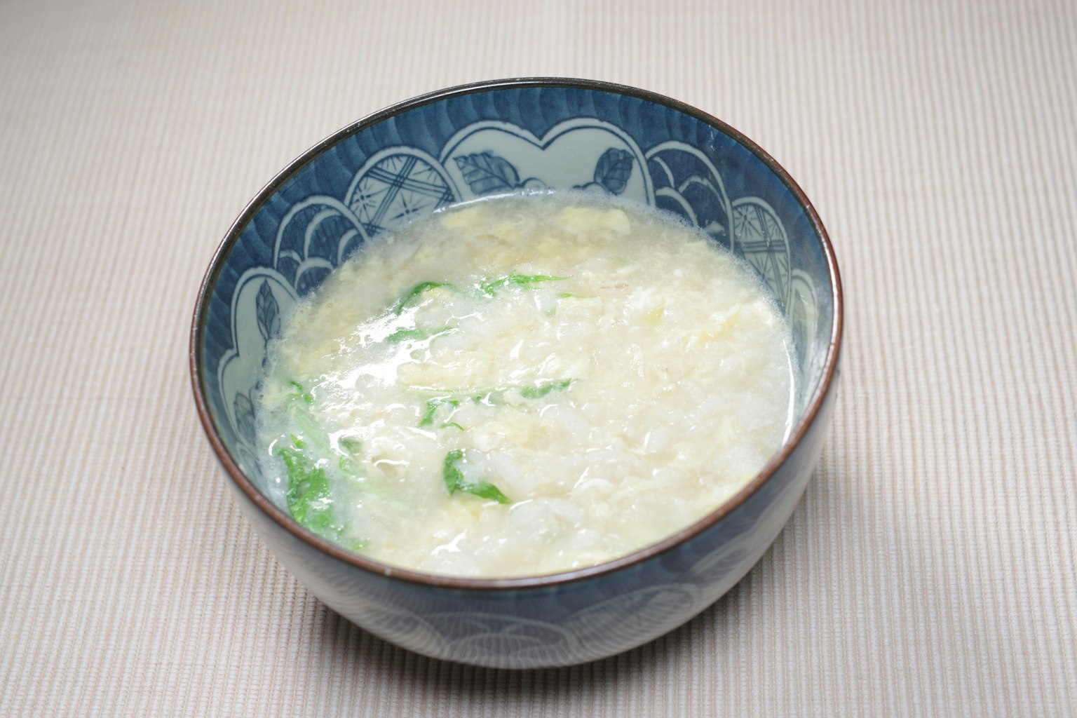 Bubur putih dengan sayuran hijau dalam mangkuk biru