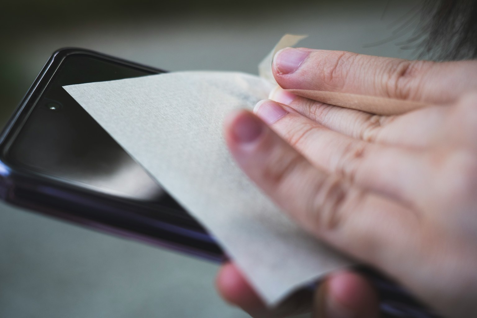 Nahaufnahme einer Hand, die ein Smartphone mit einem Tuch reinigt