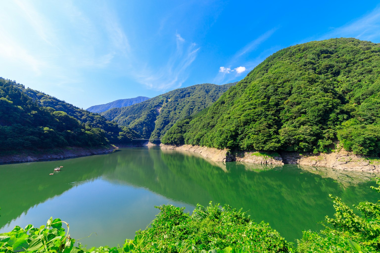 Lago panoramico circondato da montagne verdi sotto un cielo blu chiaro