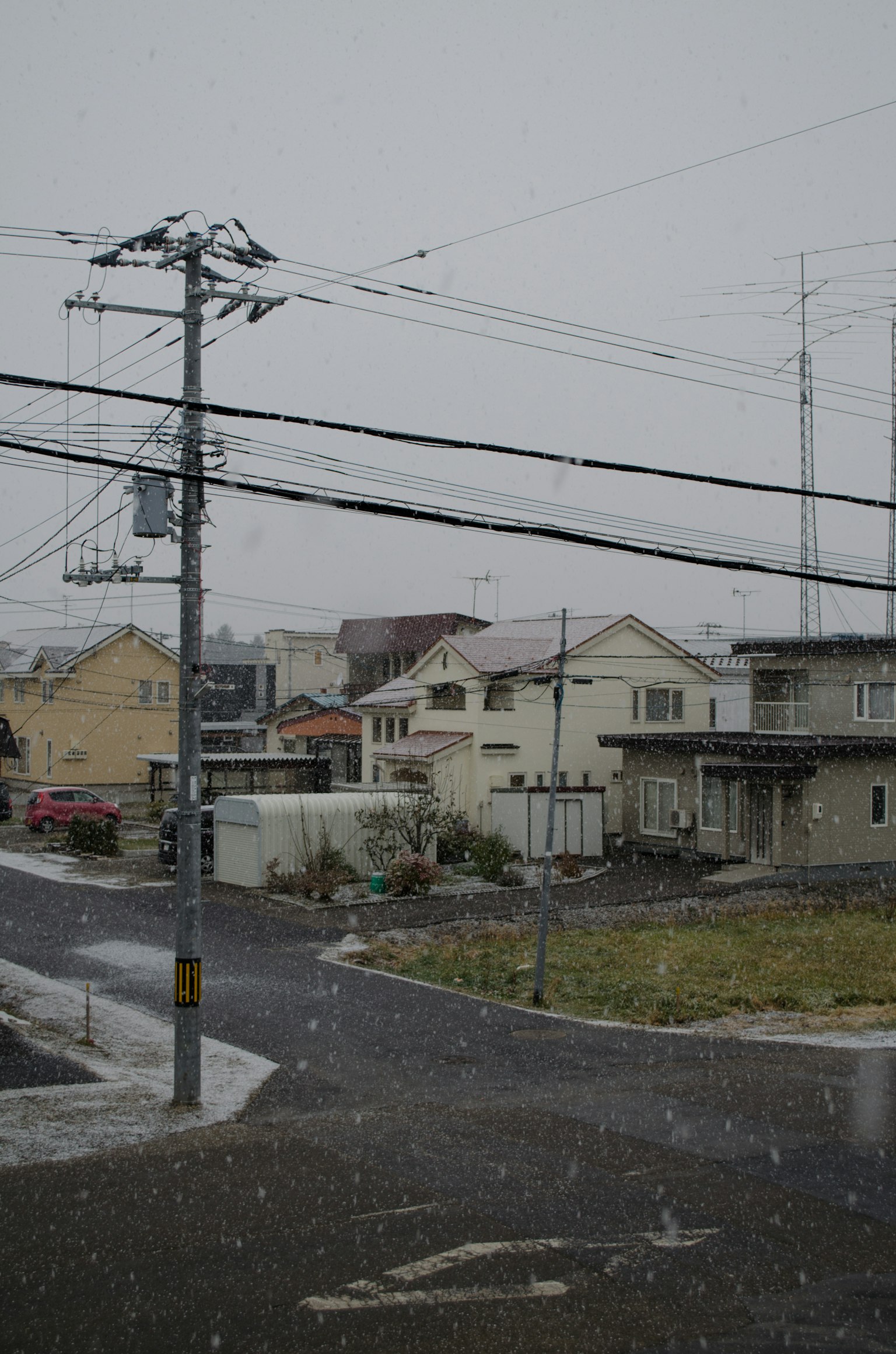 Snow falling over a residential area with houses and utility poles