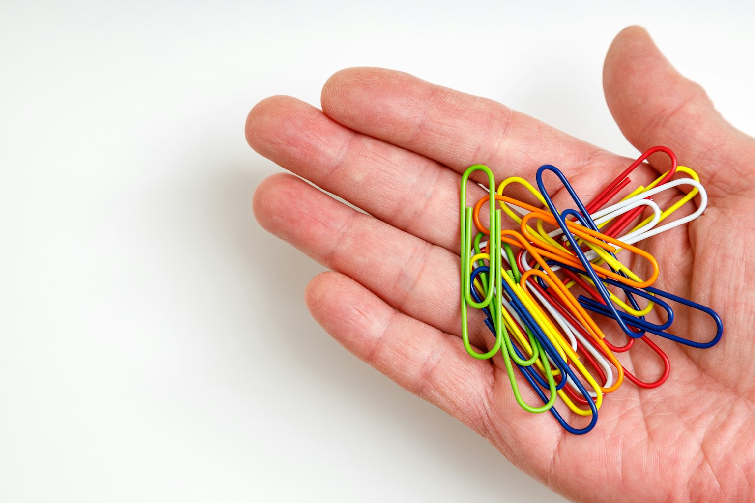 Des trombones colorés disposés sur une main ouverte