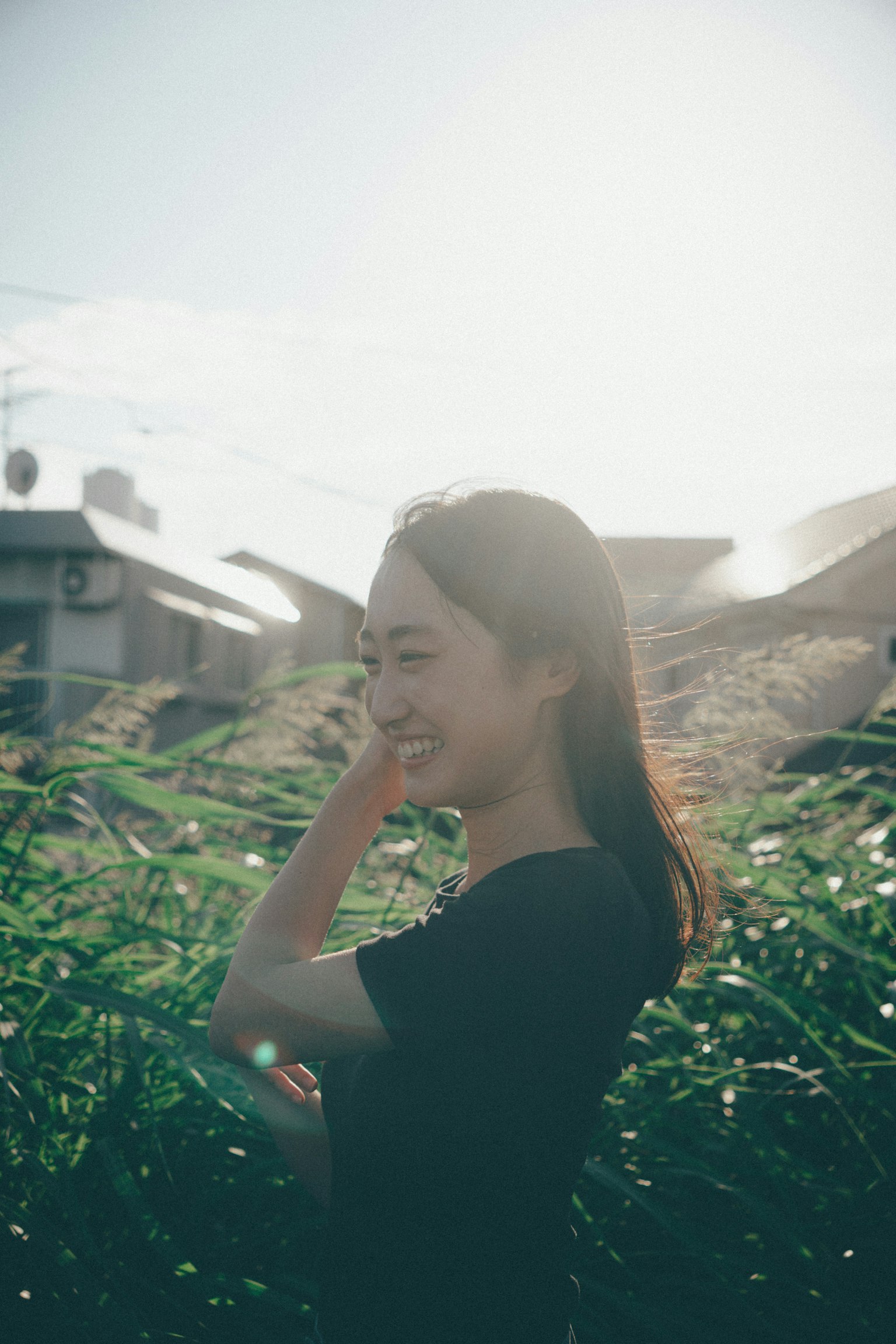 Una mujer sonriendo de perfil rodeada de hierba verde y cielo brillante