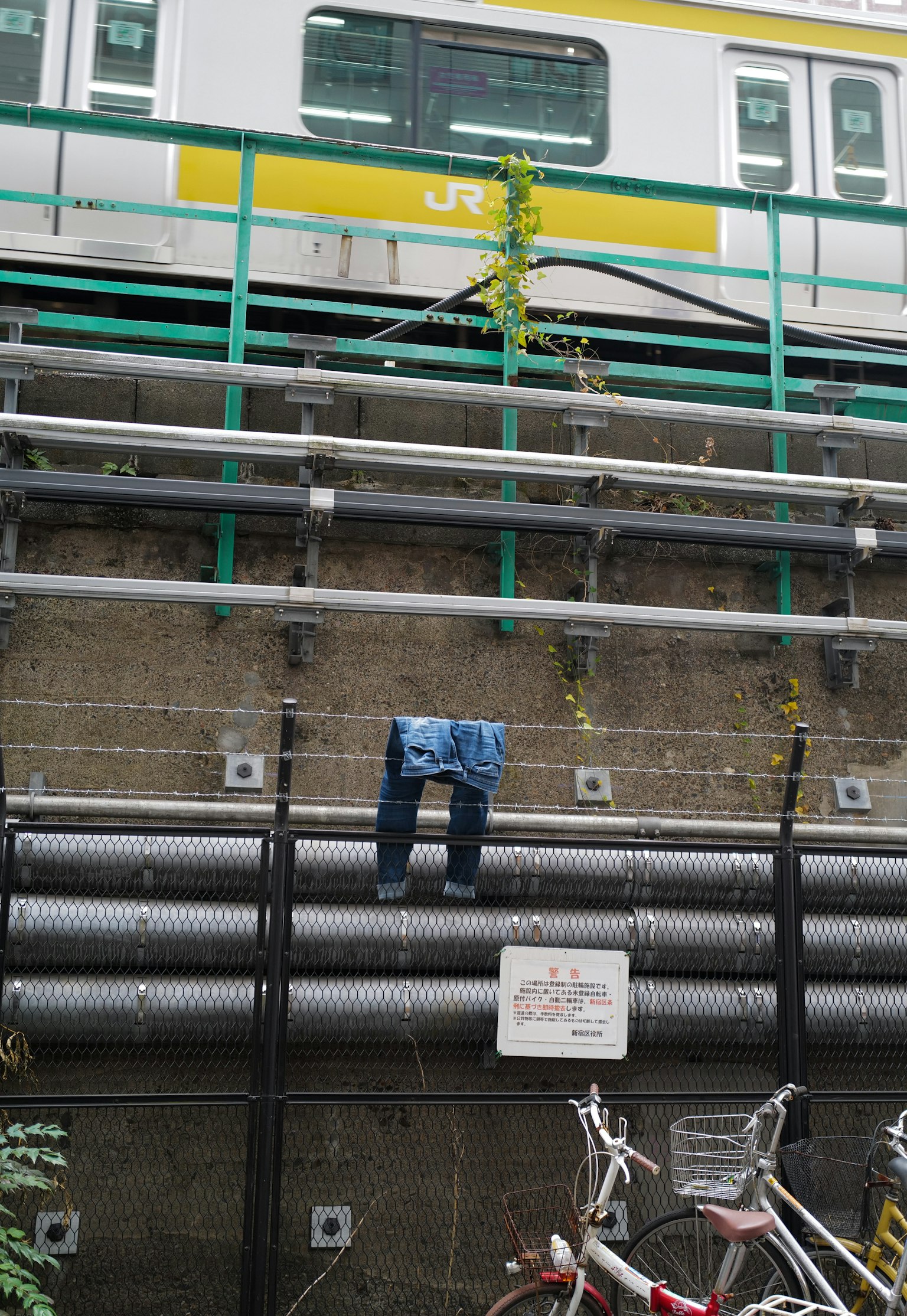 A pair of jeans hanging next to train tracks with pipes in the background