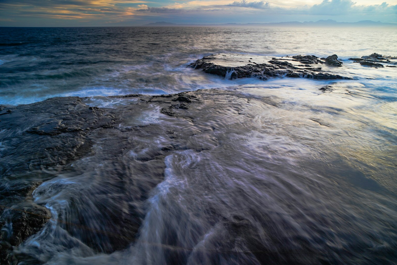 Olas rompiendo en una costa rocosa durante el atardecer