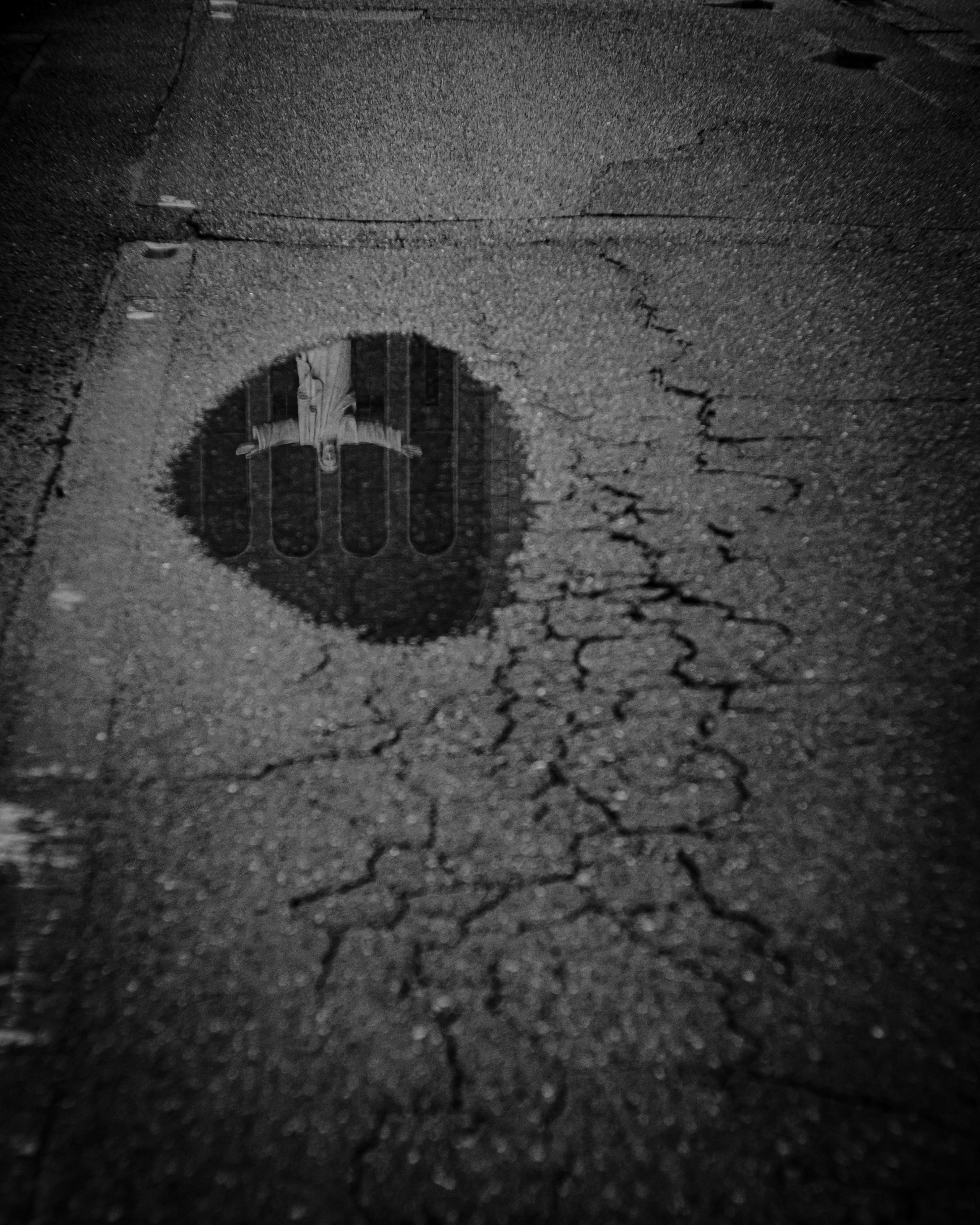 雨上がりの路面に浮かぶ円形のグレーチングと水たまり