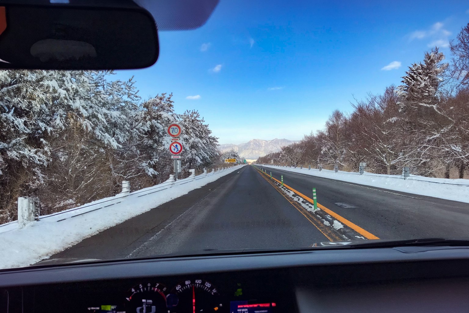Strada innevata con alberi e cielo blu