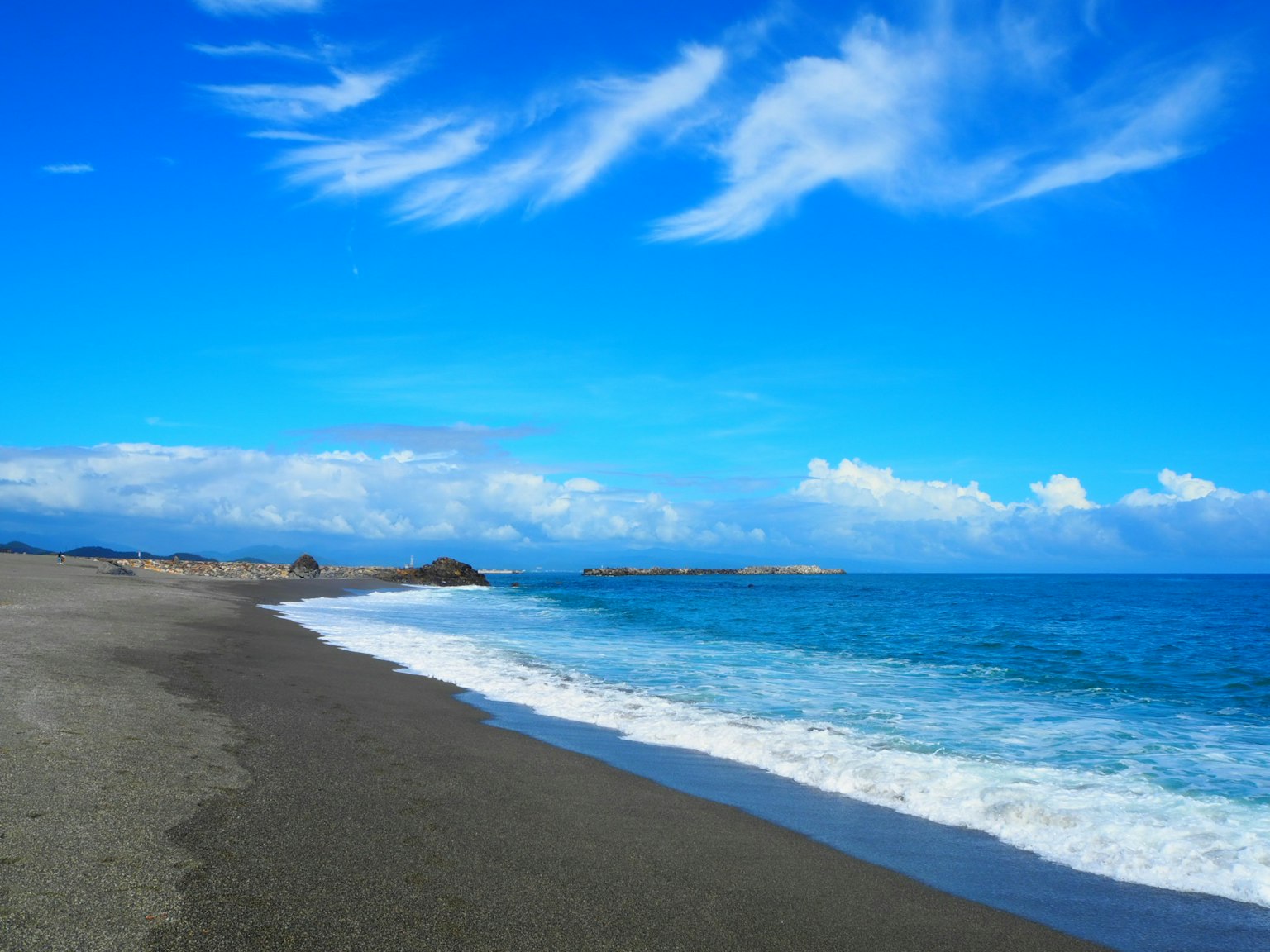 Beach scene with blue sky and white clouds gentle waves lapping on the sandy shore