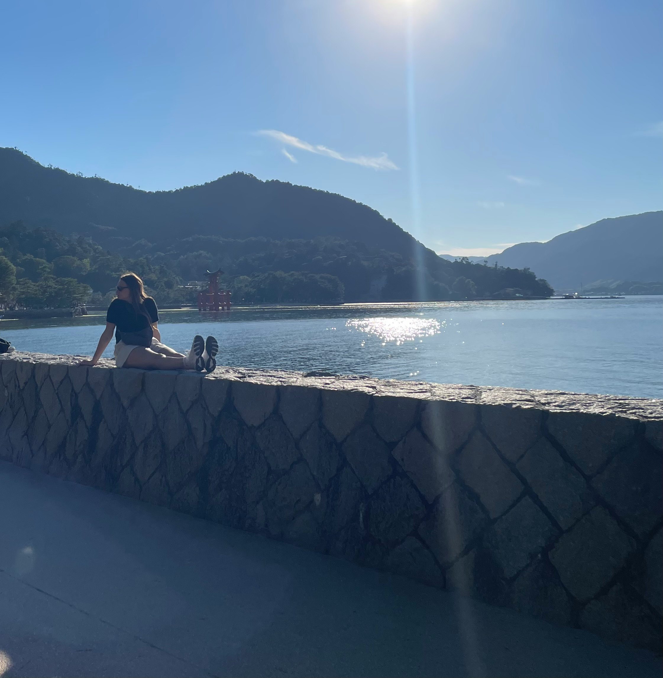 海边防波堤上坐着的人与群山景色