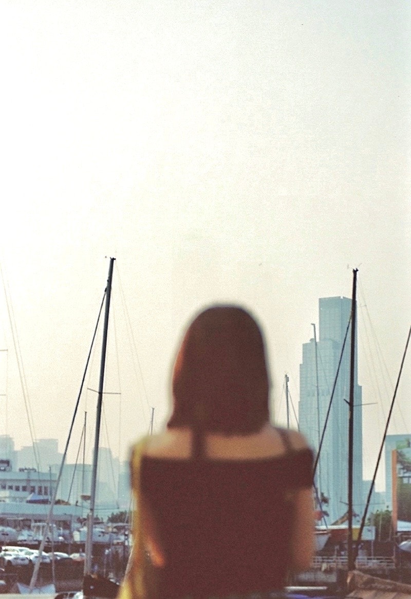เงาของผู้หญิงที่มองไปที่ท่าเรือ มีตึกระฟ้าและเรือยอชท์อยู่เบื้องหลัง