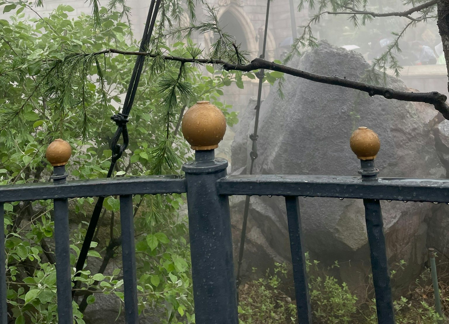蓝色铁栅栏上有金色球形装饰和绿色植物背景