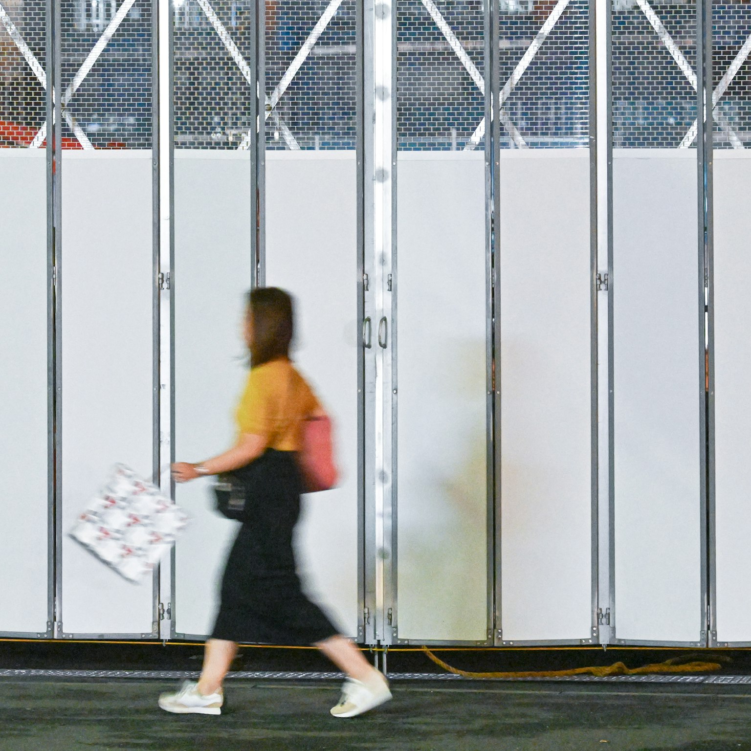 白い壁の前を歩く女性の姿が見えるシンプルな背景