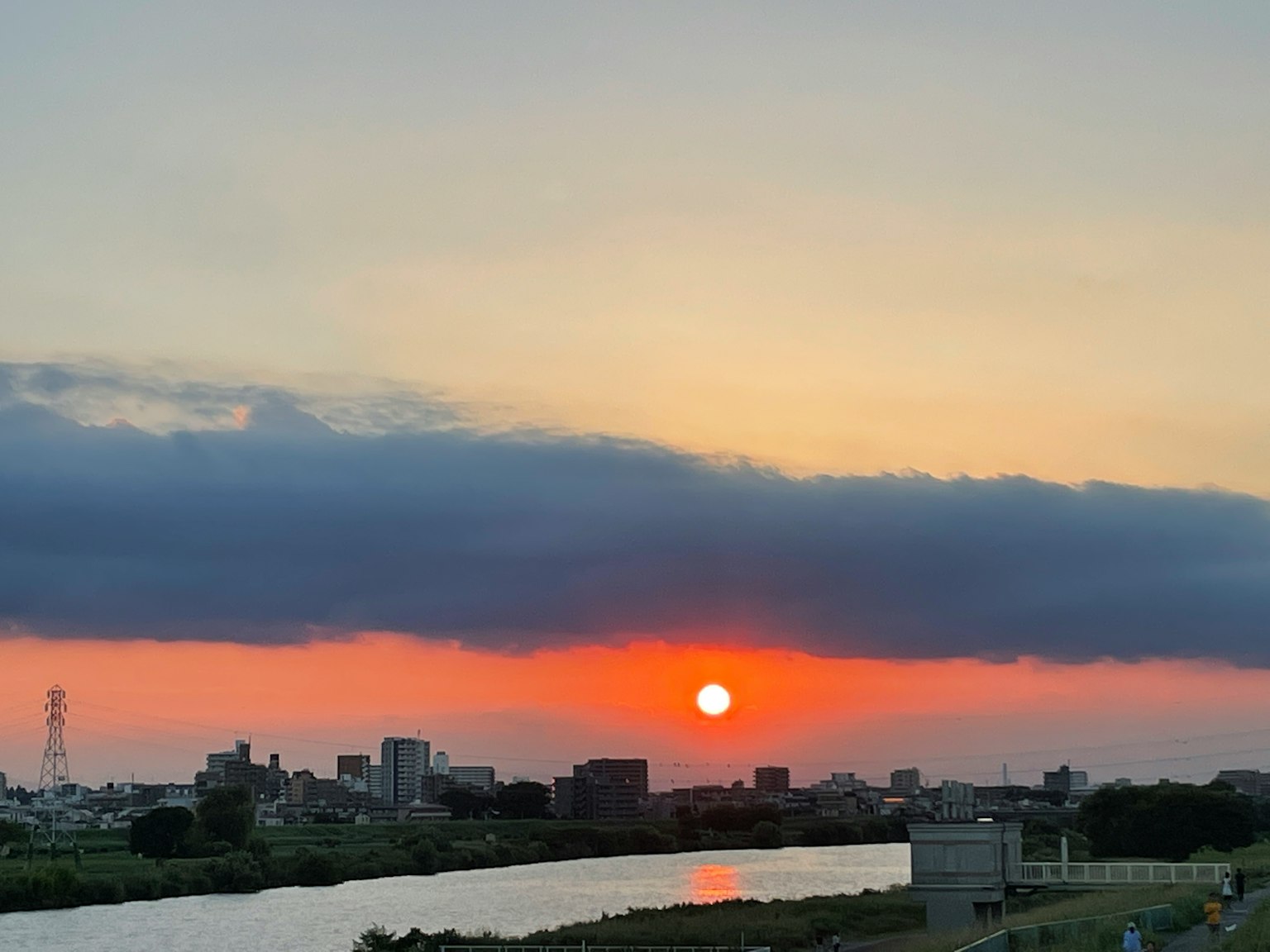 Malerscher Sonnenuntergang über einem Fluss mit Stadtsilhouette und Wolken