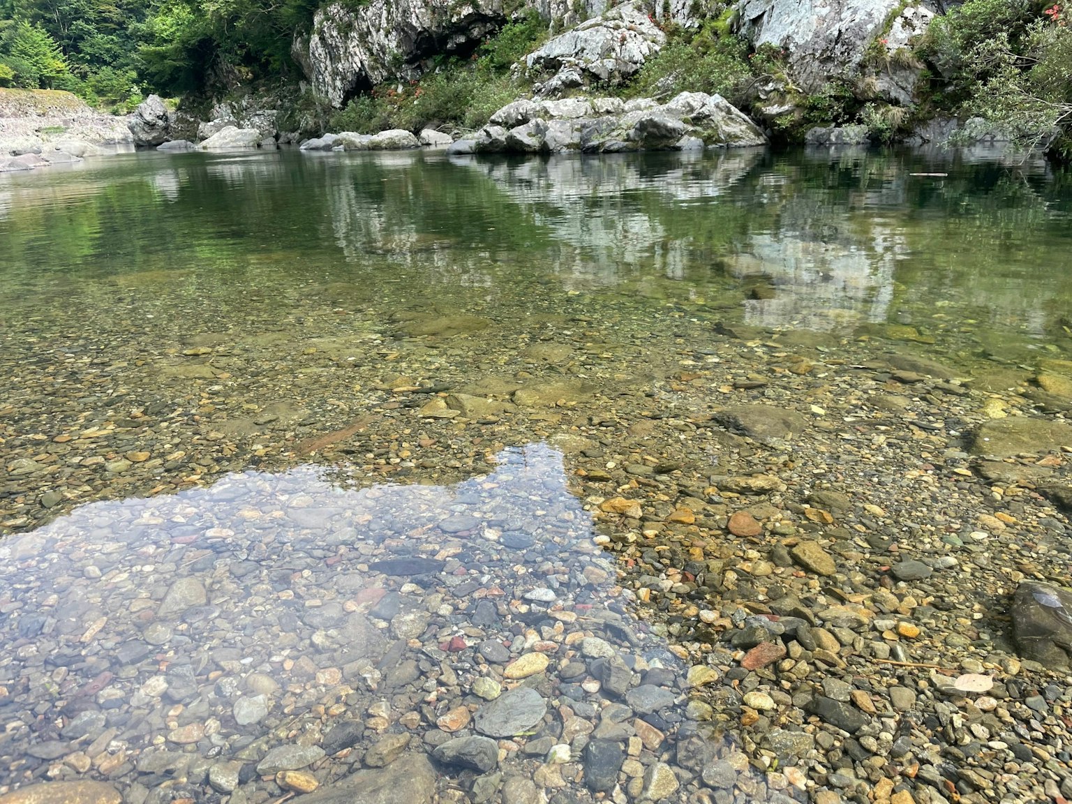 Pemandangan sungai tenang dengan air jernih dan batu yang terlihat