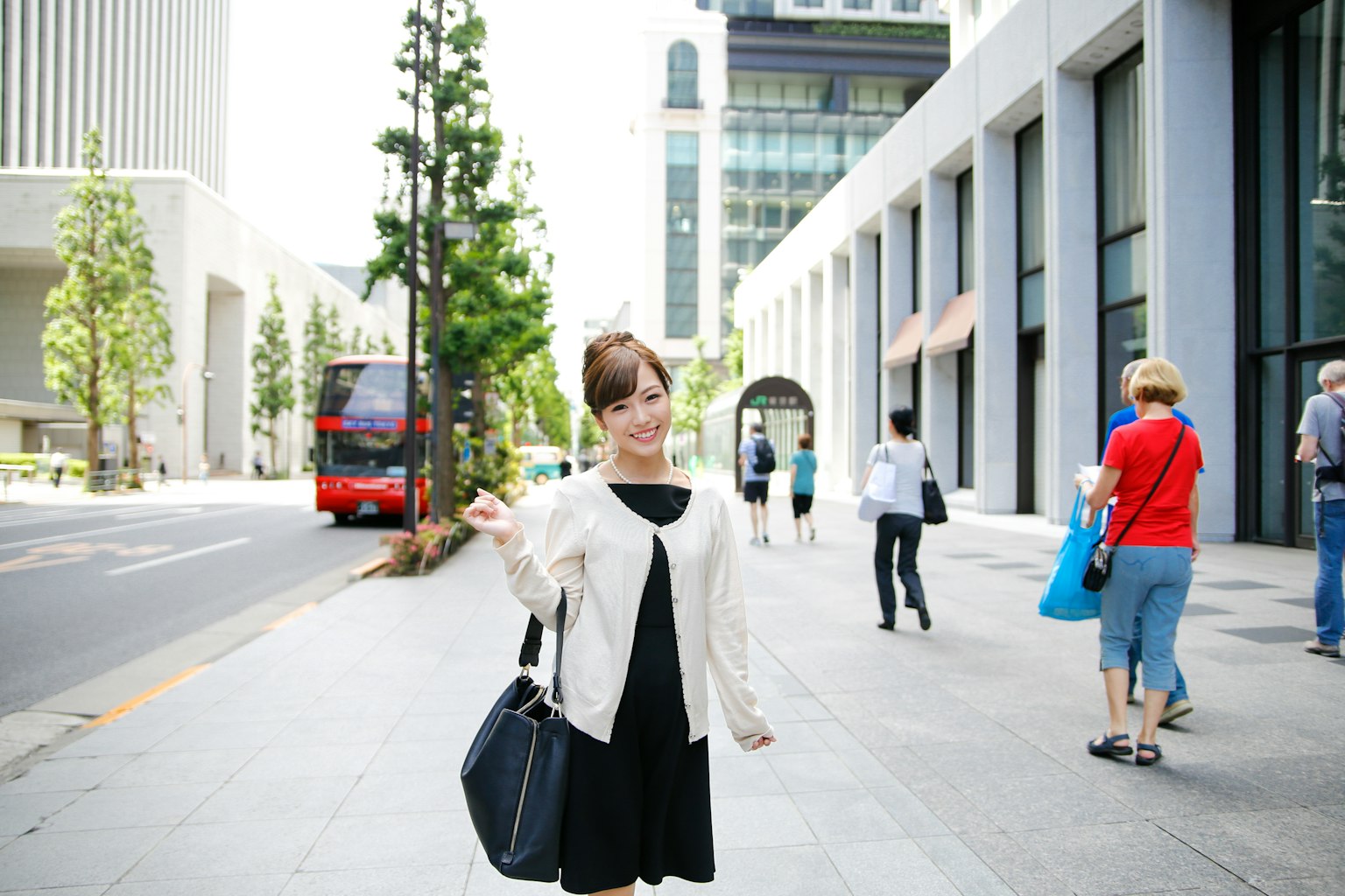Một người phụ nữ tạo dáng trên đường phố với các tòa nhà chọc trời và một chiếc xe buýt ở phía sau