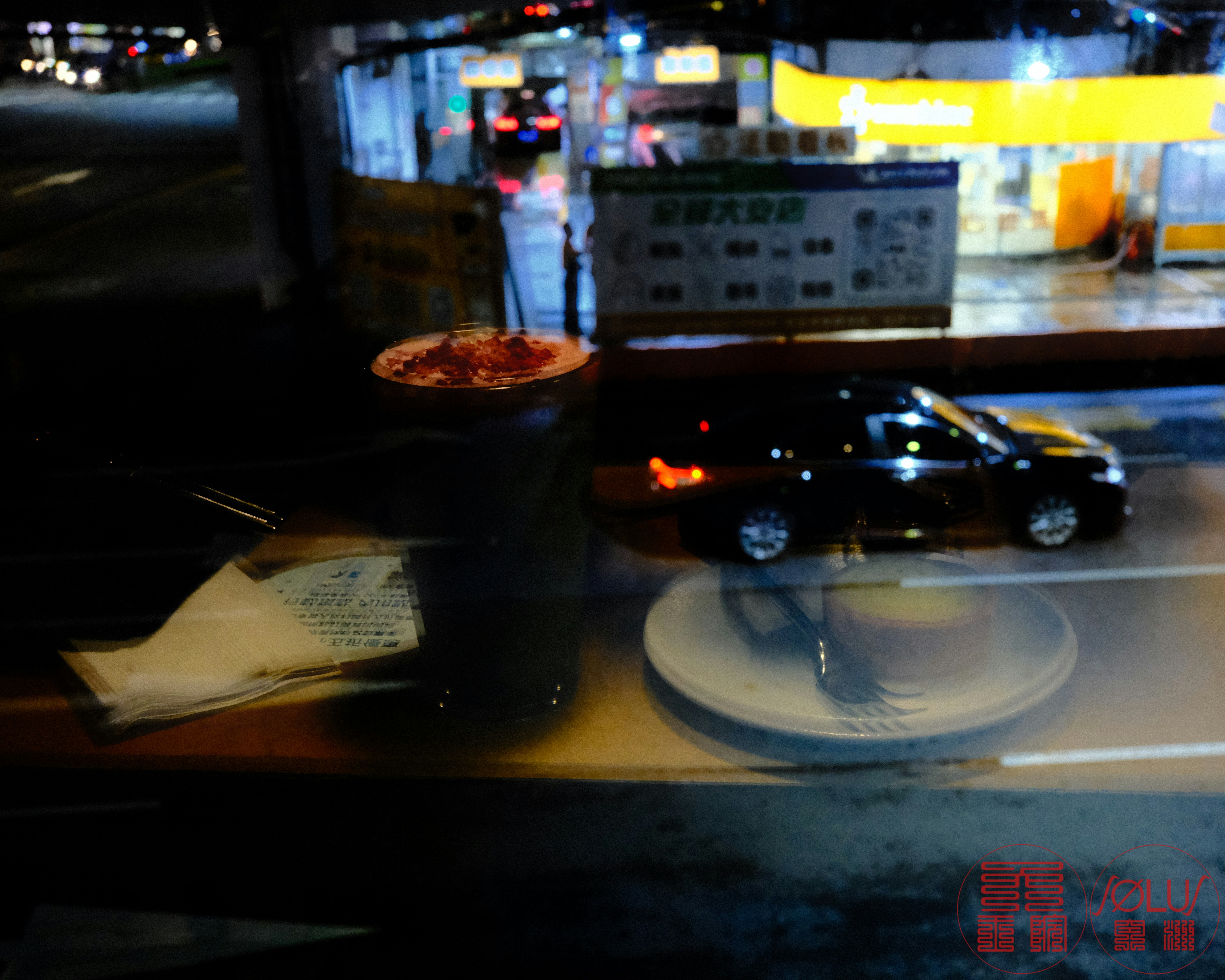 夜の店内でテーブル上の料理とコーヒー、ぼけた街の光が背景