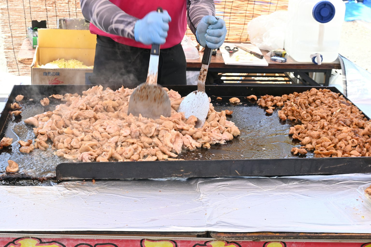 Koch, der Hähnchen auf einer großen Grillplatte an einem Imbissstand zubereitet